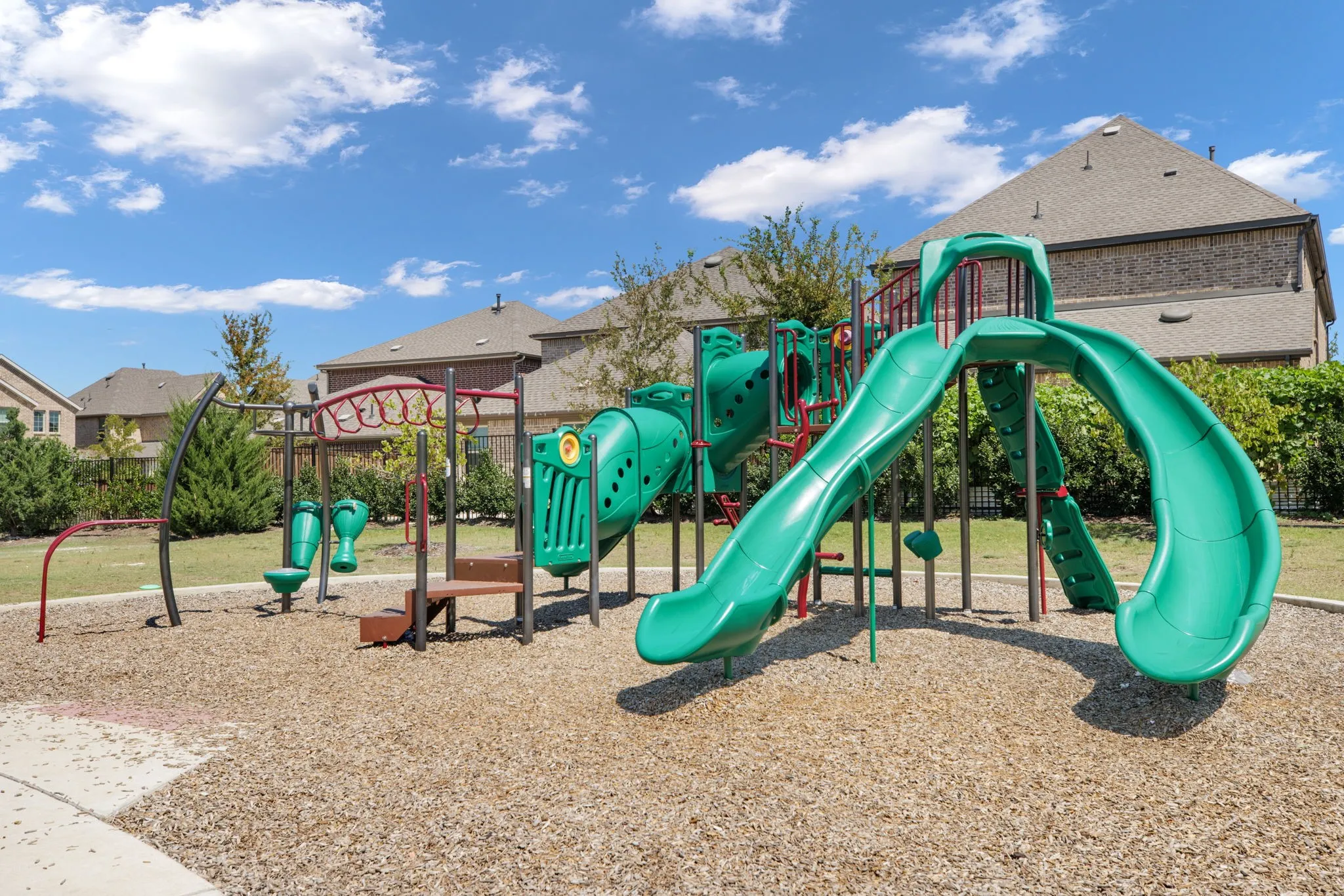 Community playground featuring a multi-level structure with slides, climbing elements, and a wood chip surface