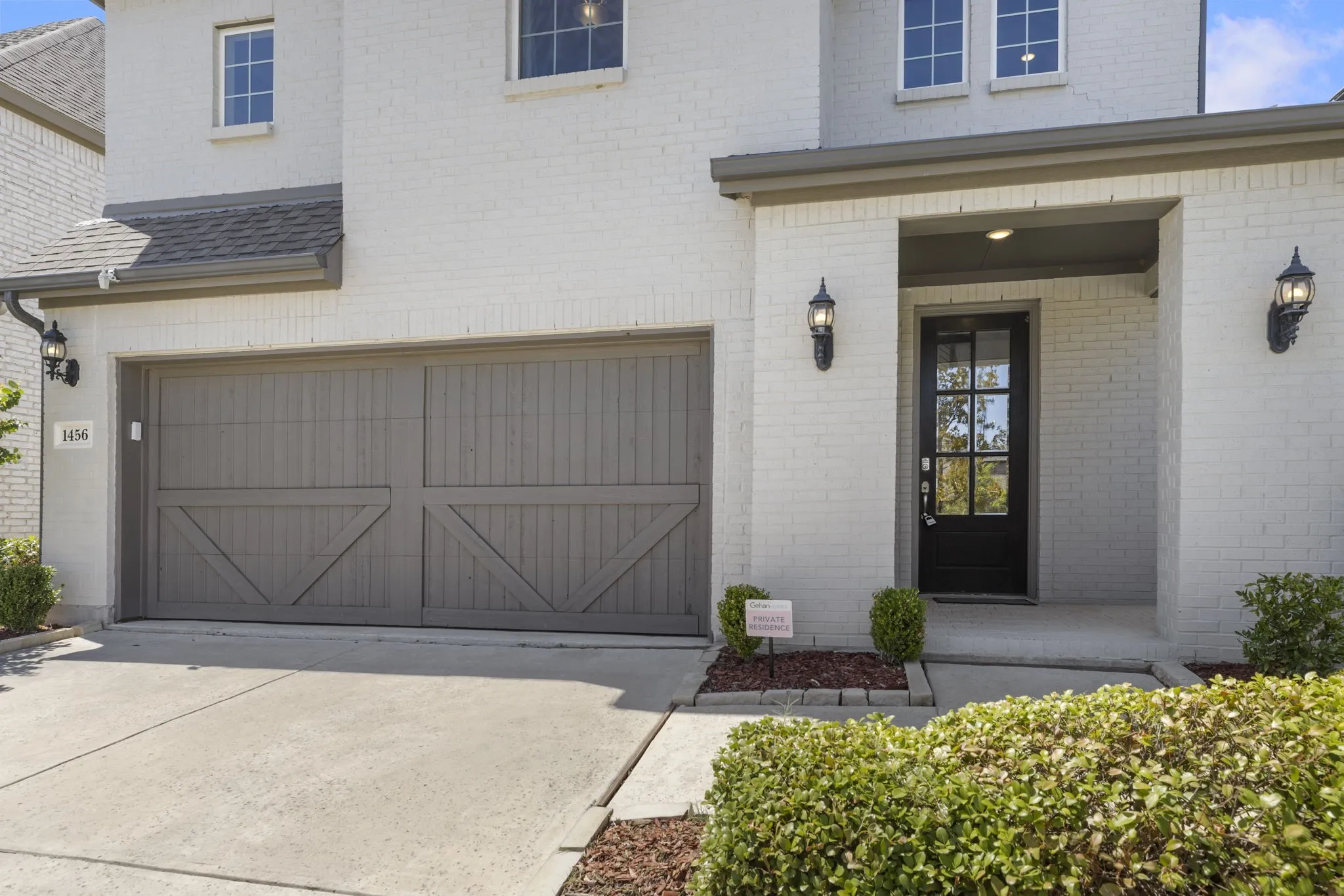 Brick exterior with white finish, covered entry, black paneled front door with glass inserts, and two-car garage with decorative doors