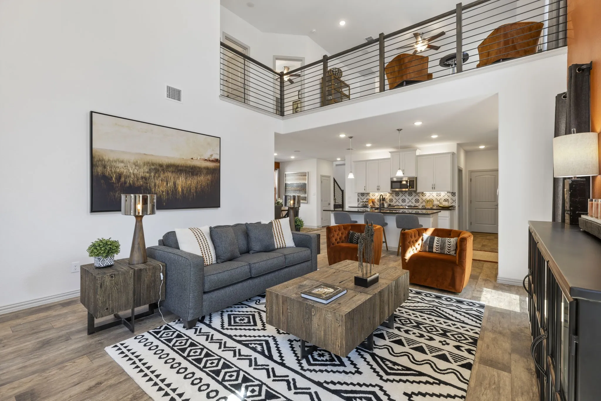 Open-concept living area featuring high ceilings, wood-finish flooring, a kitchen with a patterned tile backsplash, a tiered island, and a loft with horizontal railings