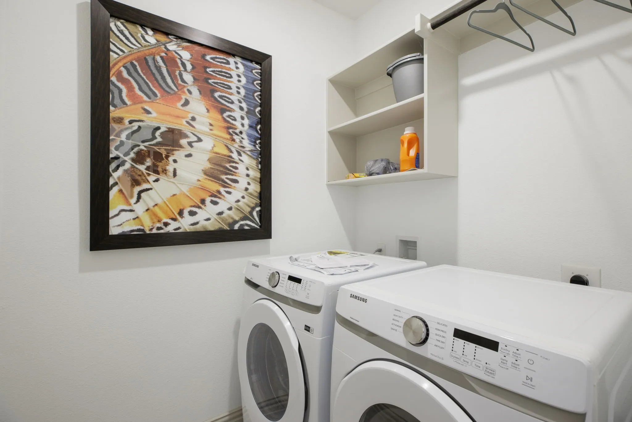 Integrated laundry area featuring built-in shelving, a hanging rod, and white appliances