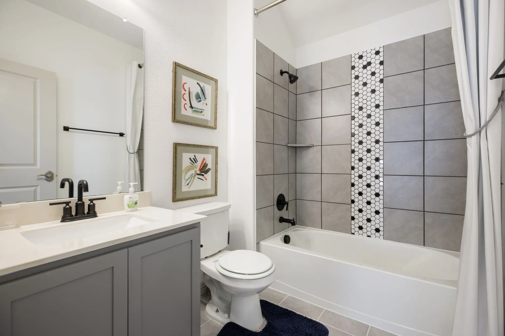 Bathroom featuring a single vanity with stone countertop, matte black fixtures, and a shower/tub combination with tiled surround and decorative accent