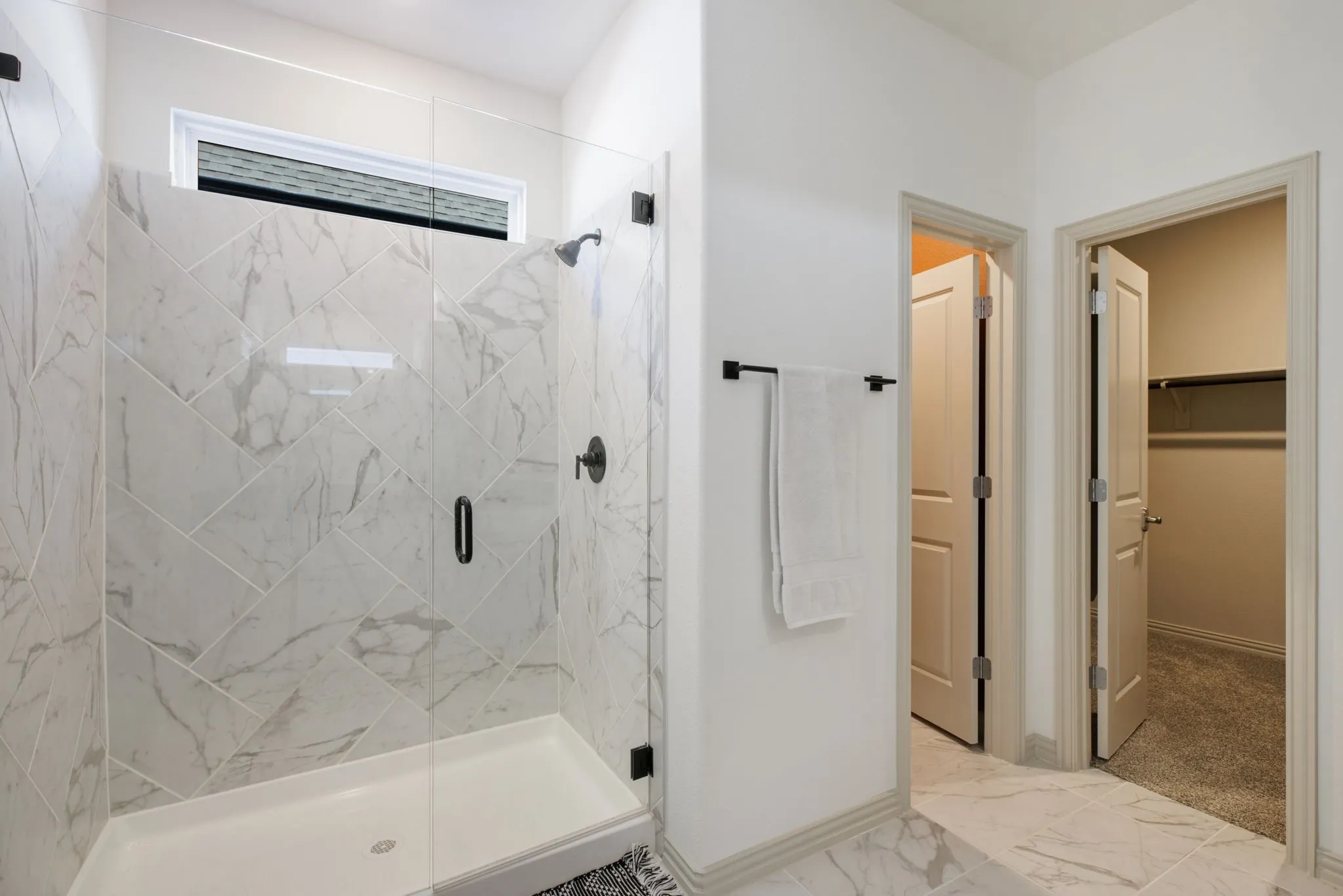 Glass-enclosed shower with a white tile surround in a herringbone pattern and matte black fixtures