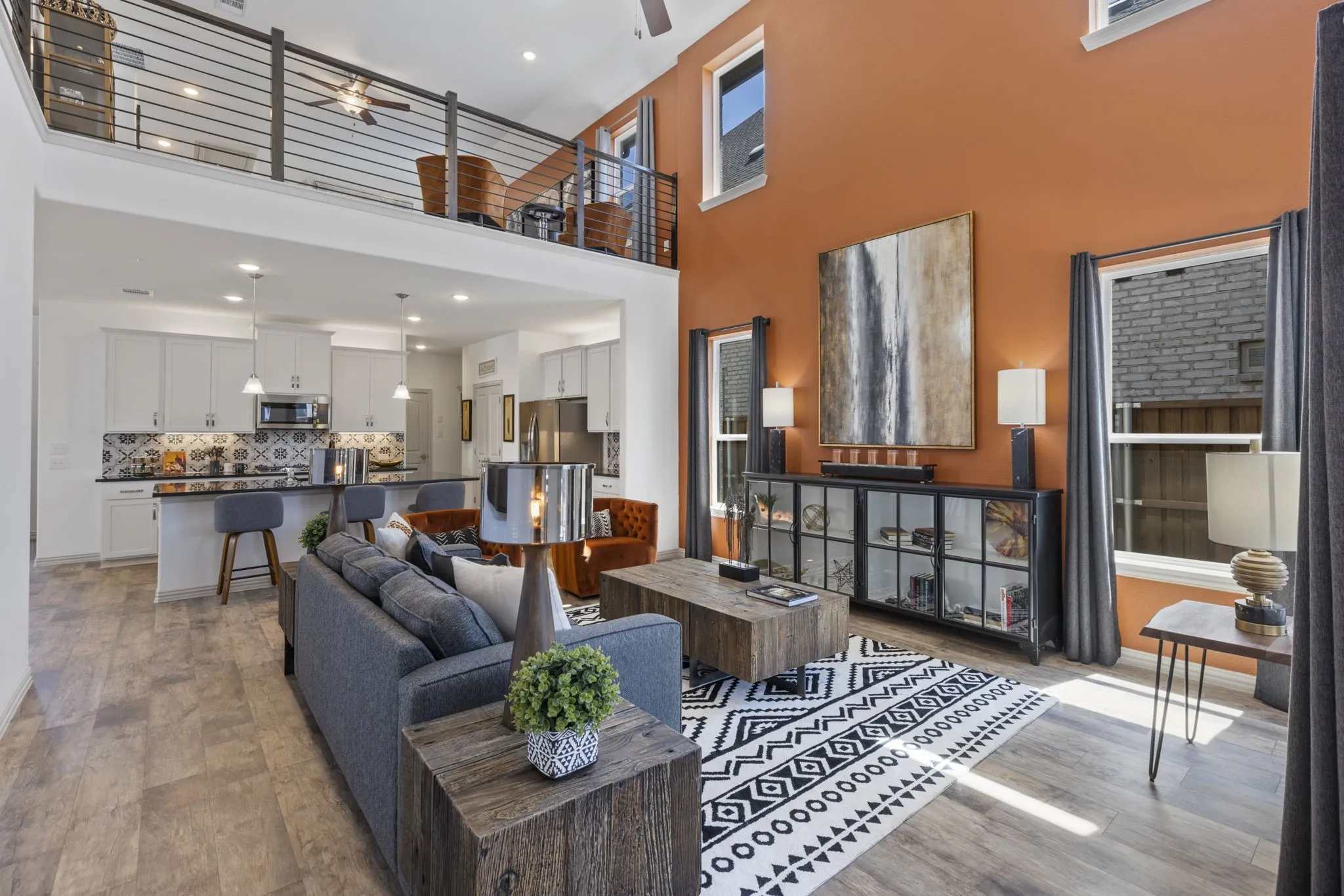 Soaring ceilings, wood-finish flooring, two-story windows, open-concept kitchen with a breakfast bar, and an upper-level loft with metal railings