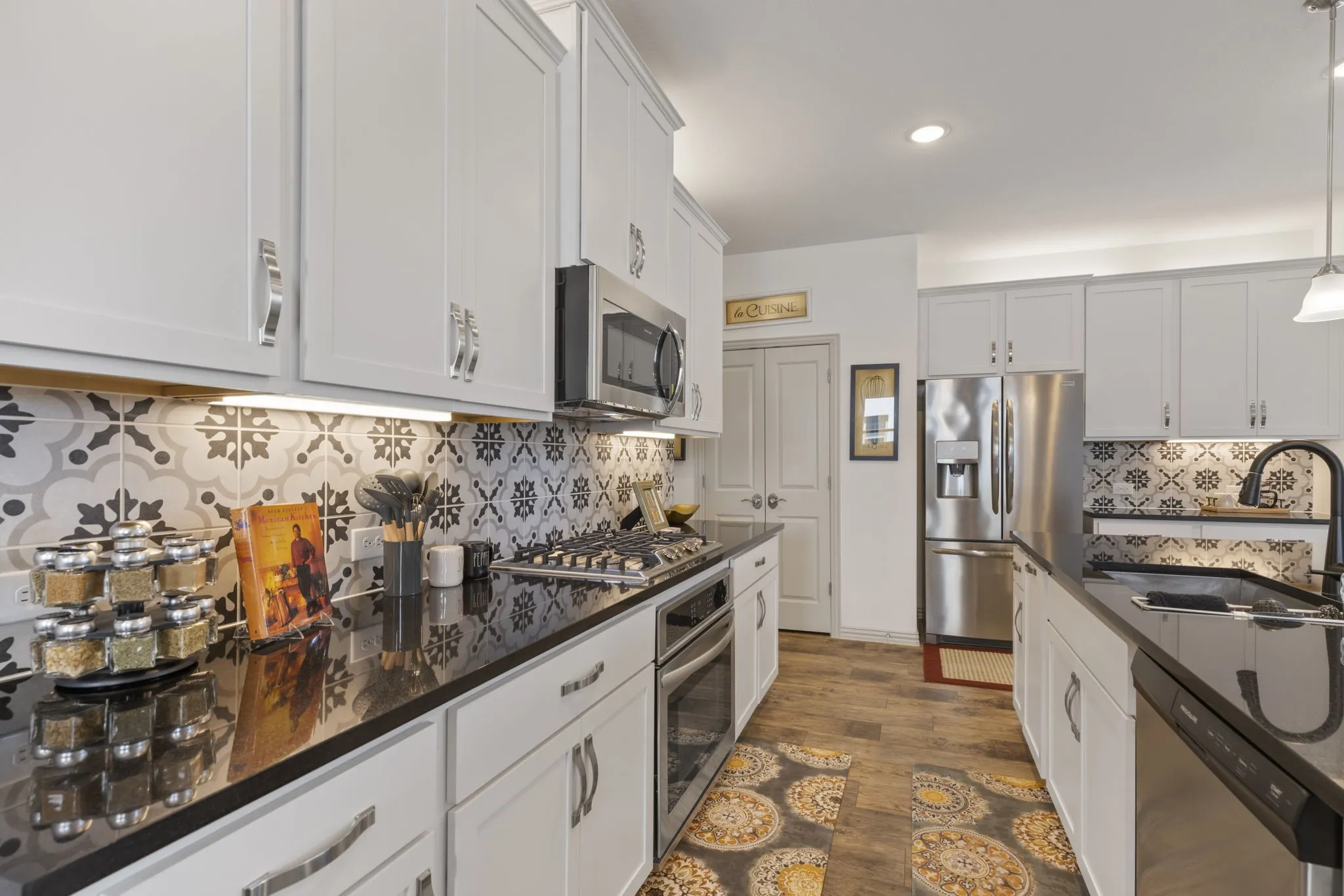 White shaker cabinetry with chrome hardware, dark countertops, patterned tile backsplash, wood-finish flooring, and stainless steel appliances