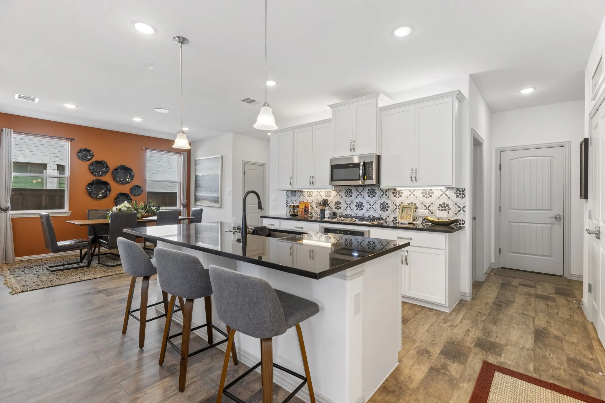 Open-concept kitchen and dining area featuring white cabinetry, a large kitchen island with a black countertop, stainless steel appliances, and wood-finish flooring