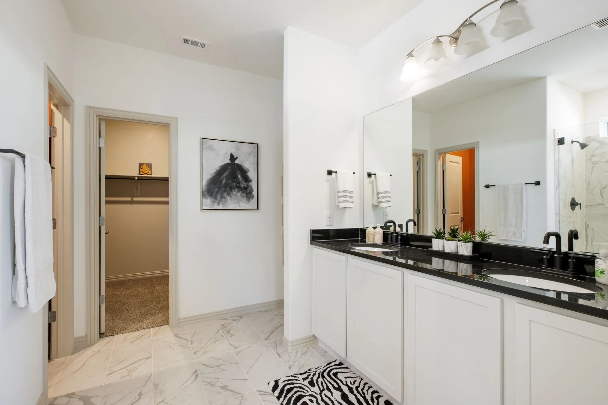 Dual vanity with white cabinetry and dark countertops, large mirror, and tiled flooring