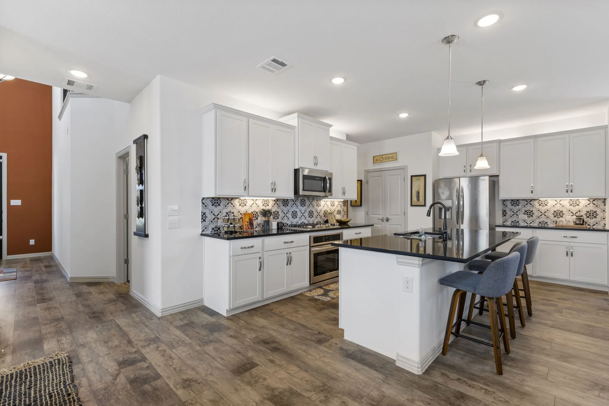 Kitchen featuring wood-finish flooring, white cabinetry, black countertops, and a patterned tile backsplash