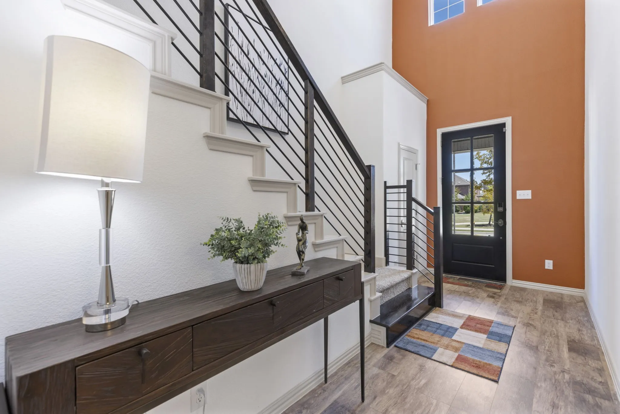 Entryway featuring a high ceiling, transom windows, wood-finish flooring, a black paneled door with glass inserts, and a staircase with metal railings