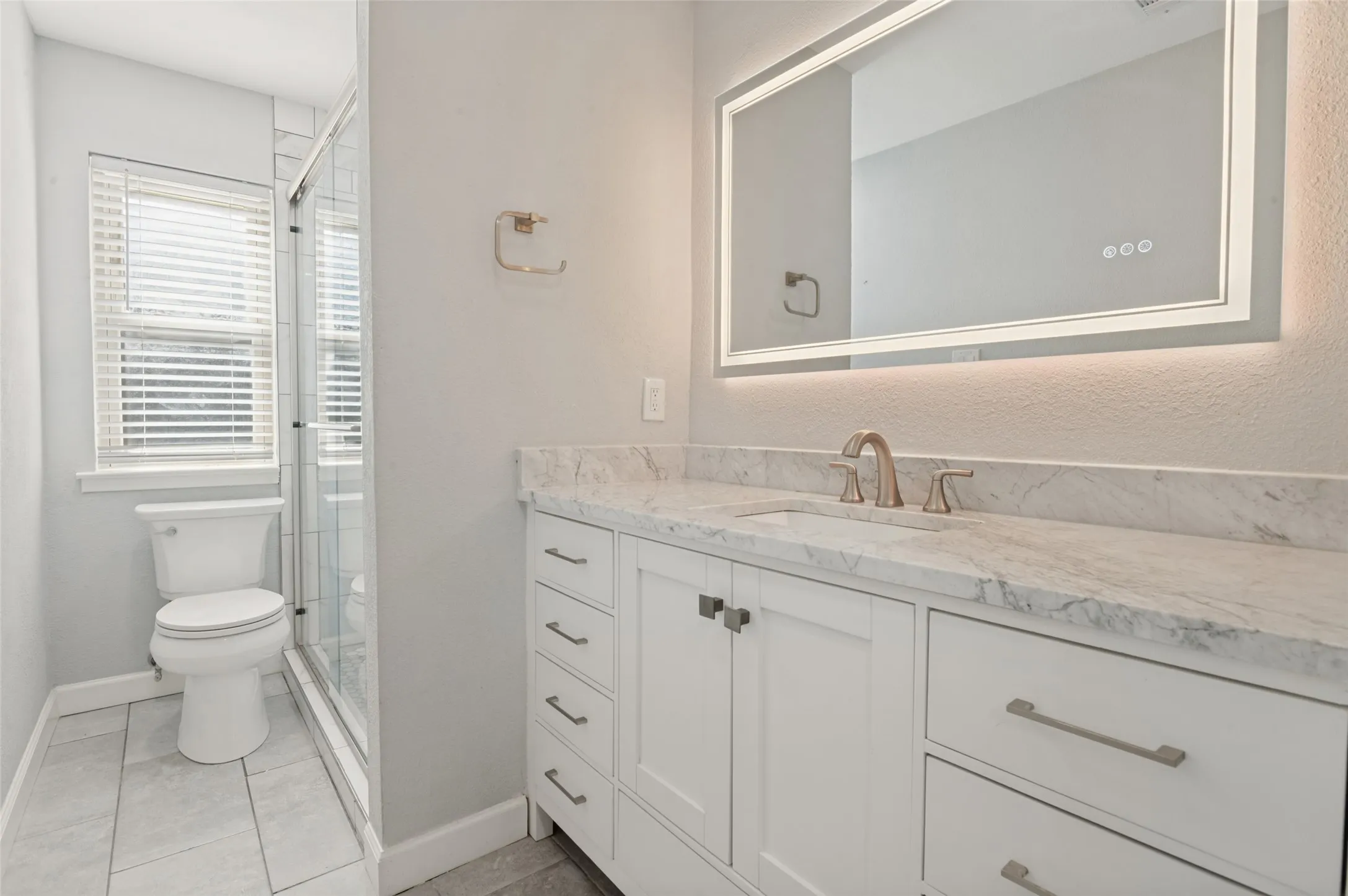 White vanity with a stone countertop, an illuminated mirror, and a glass-enclosed shower
