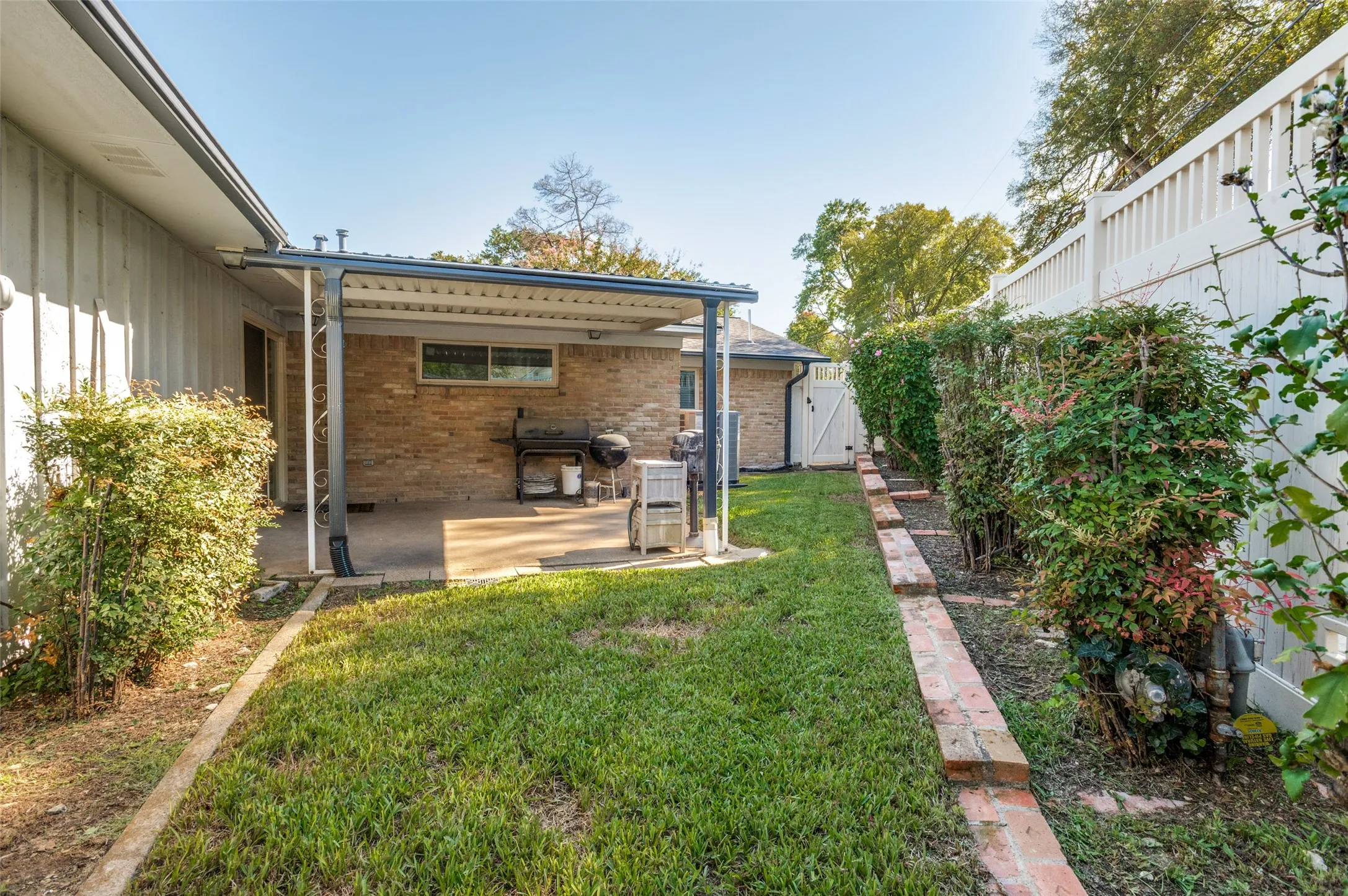 Covered patio with a concrete slab, brick exterior, and a white privacy fence