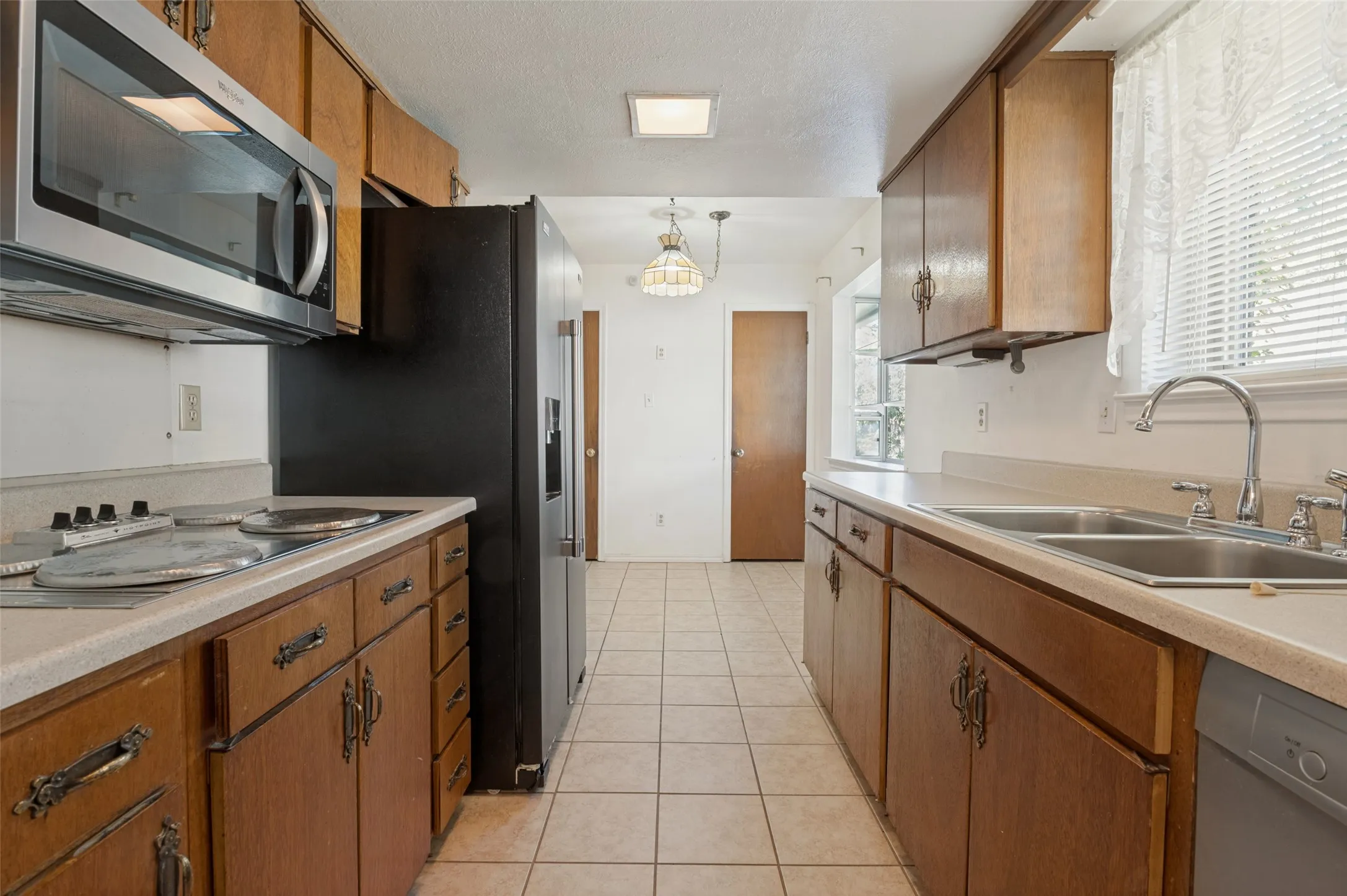 Galley kitchen featuring wood cabinetry, laminate countertops, a stainless steel microwave, and tile flooring