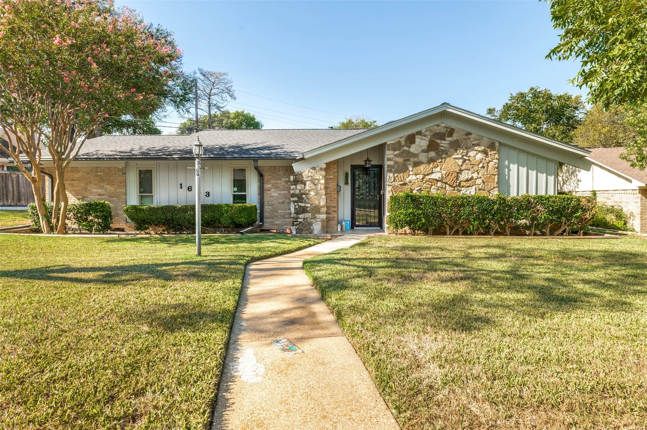 Single-story residence featuring a combination of brick and stone facade, a gabled roofline, and a concrete pathway leading to the front entry