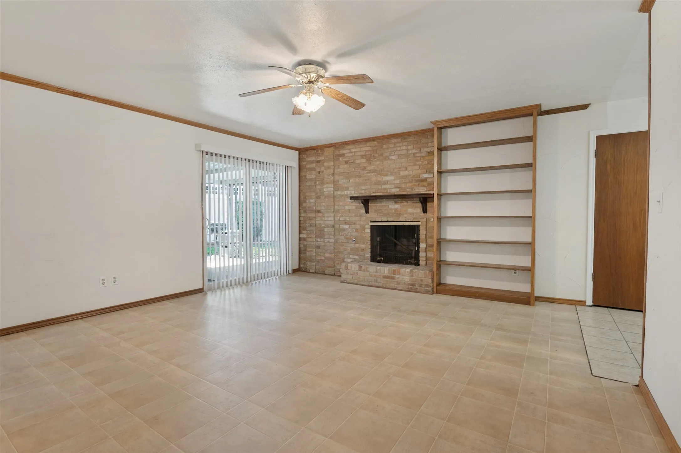Brick fireplace with dark wood mantel, built-in shelving, ceiling fan, and tile flooring