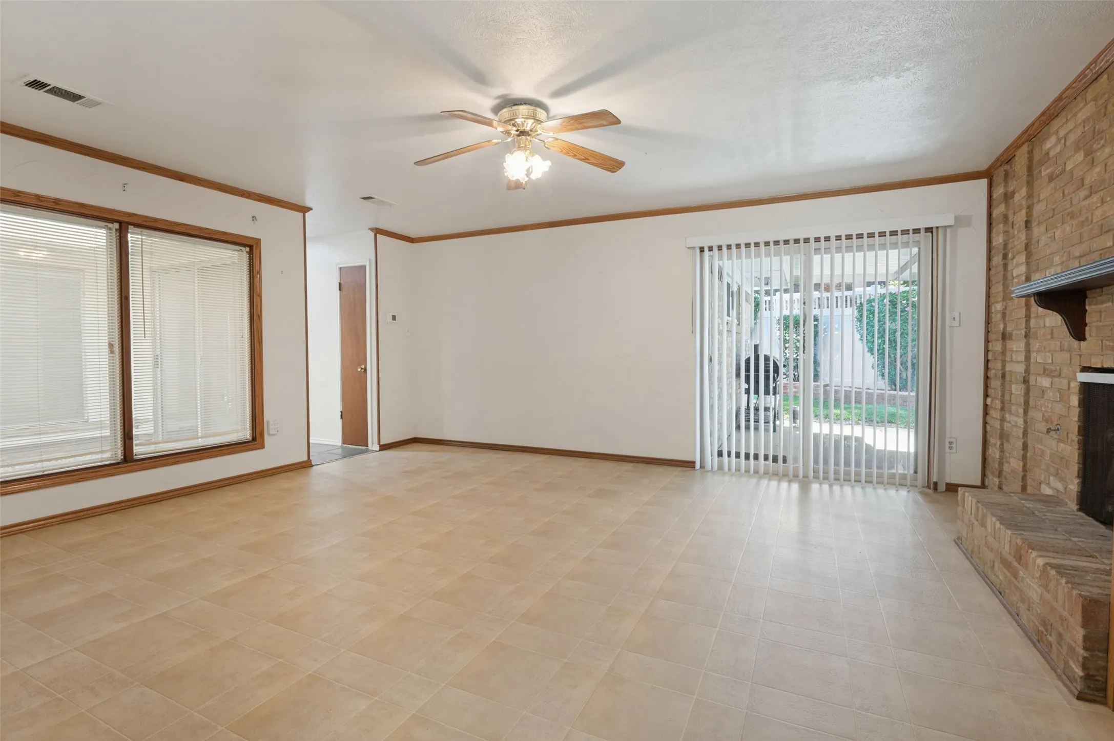 Spacious room featuring tile flooring, a brick fireplace, a ceiling fan with integrated lighting, and a sliding glass door leading to the exterior