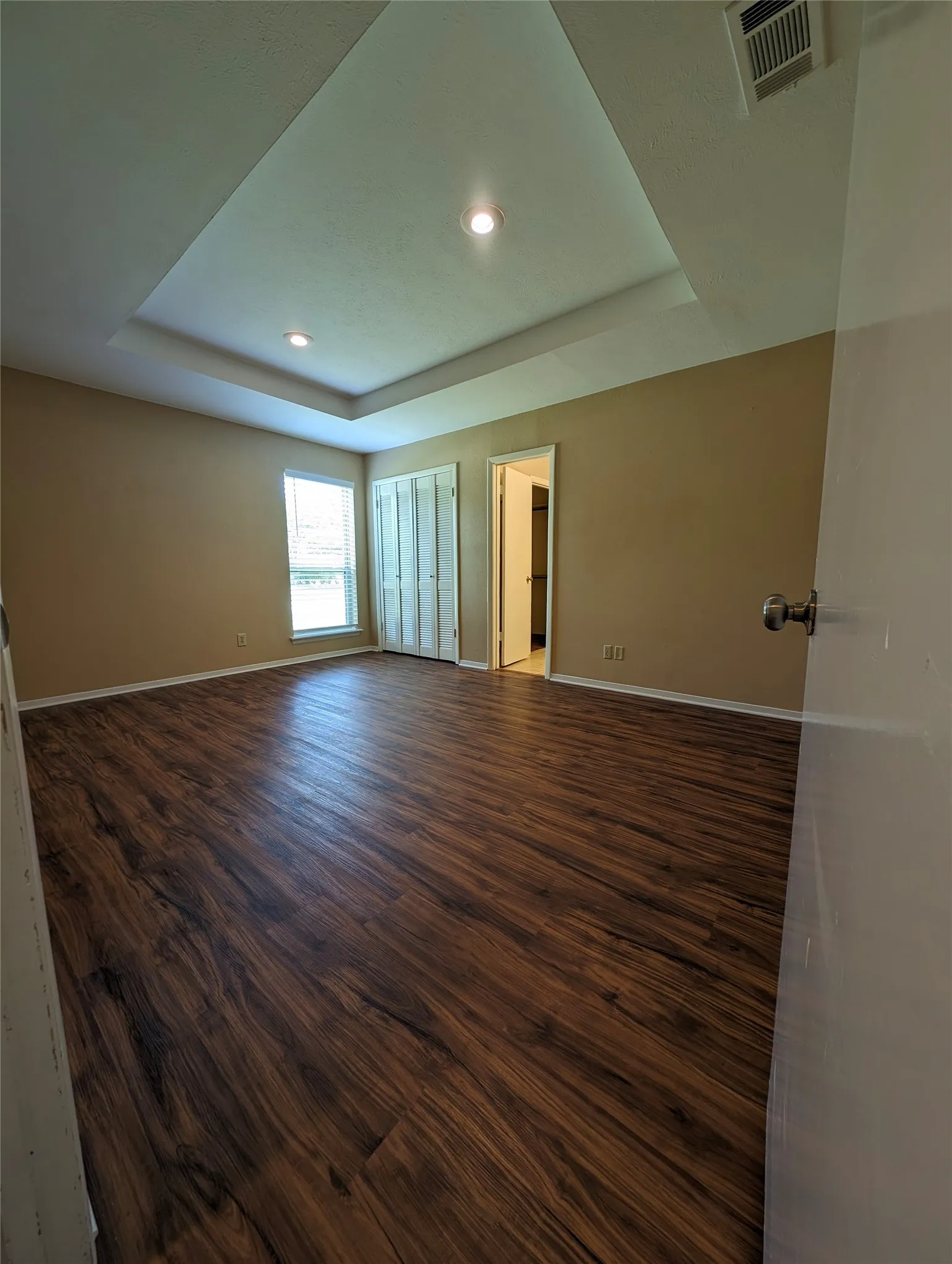 Wood-finish flooring with a decorative tray ceiling and recessed lighting