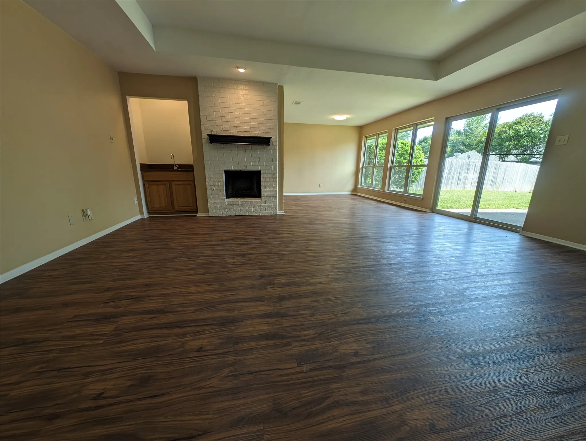 Spacious living area featuring wood-finish flooring, a white brick-faced fireplace, a built-in wet bar with wood cabinetry, and extensive window panels