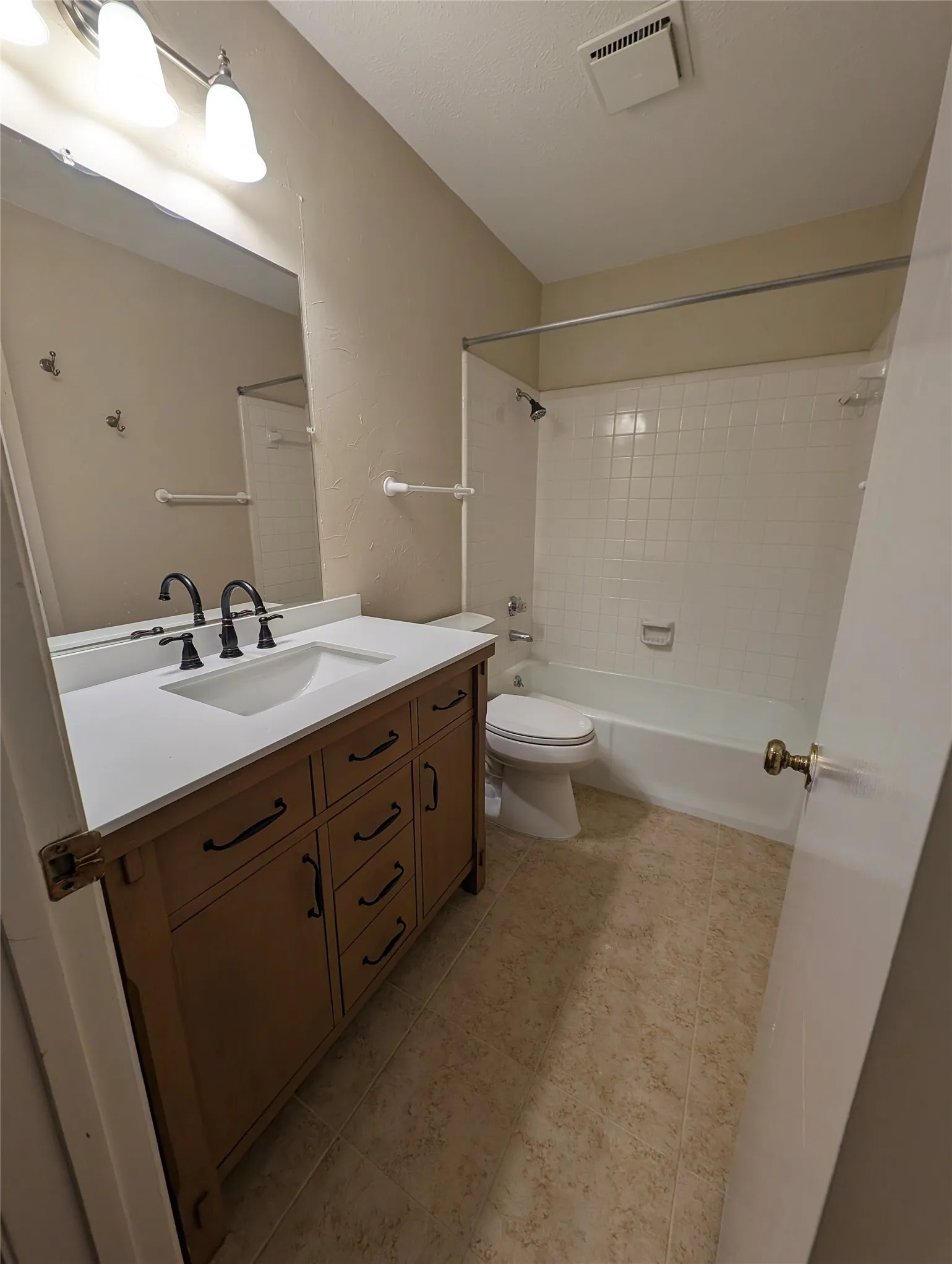 Bathroom featuring a wood-finish vanity with a white countertop and integrated sink, matte black faucet, and tiled flooring