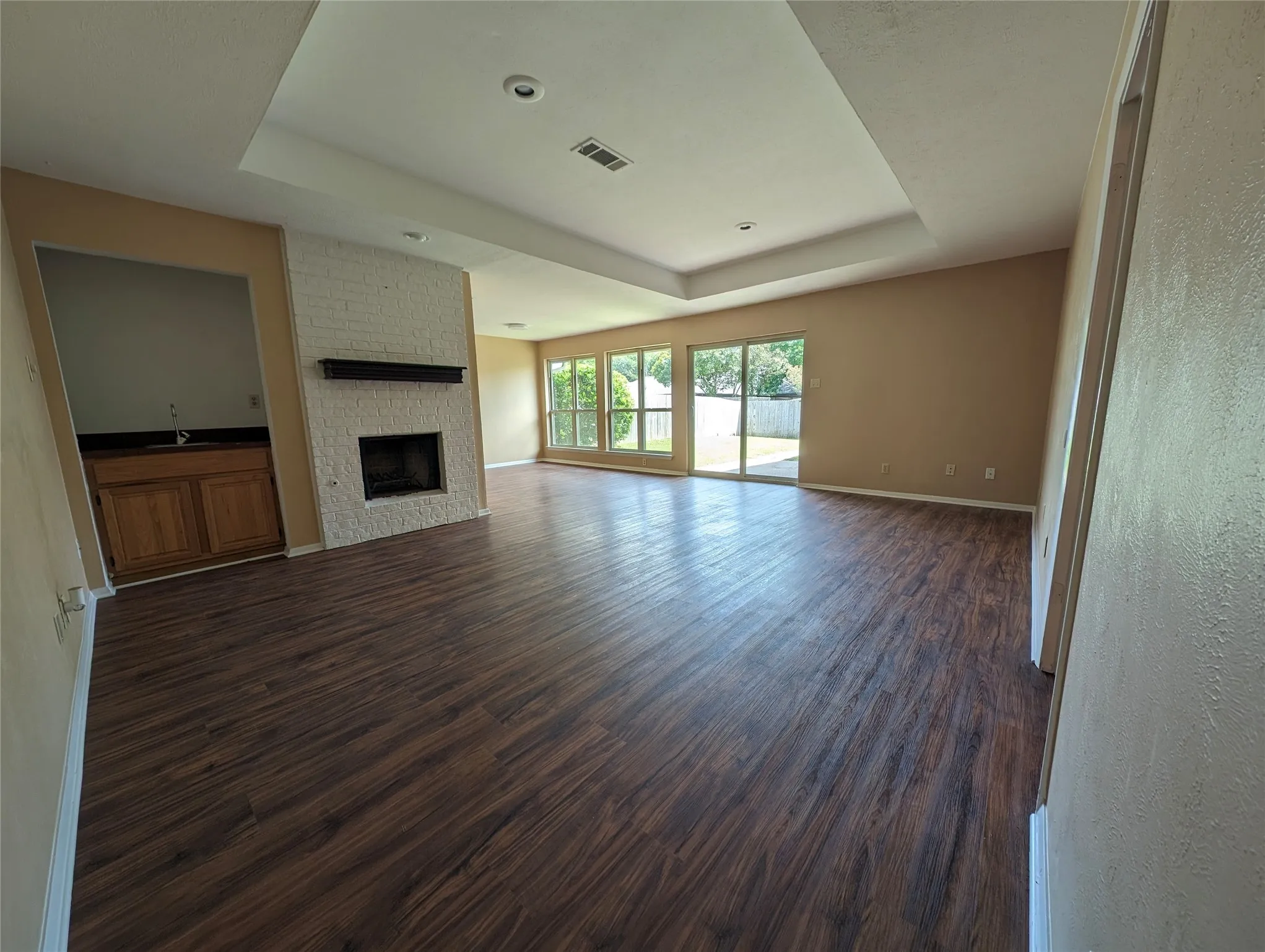 Spacious living area featuring wood-finish flooring, a white brick fireplace with a dark mantel, and recessed lighting