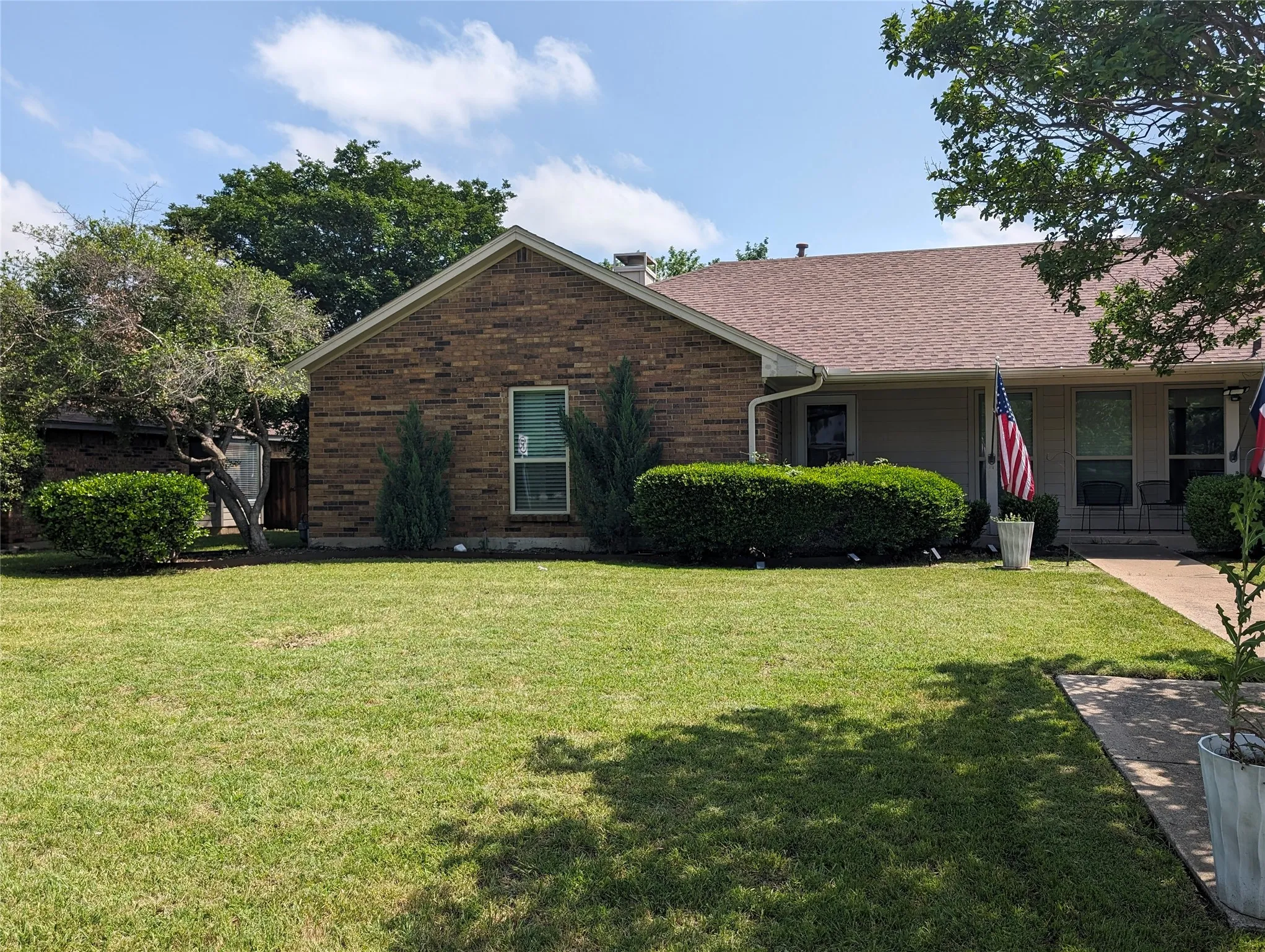 Brick exterior with a gabled roofline, mature trees, and an expansive front lawn