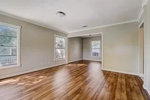 Bright corner room showcasing gleaming wood-finish flooring throughout, abundant natural light from multiple windows with transom detailing, clean white crown molding, and neutral wall finishes ideal for versatile decorating