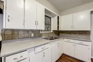 Kitchen featuring wood-finish flooring, white cabinetry, light-toned countertops, and a tiled backsplash
