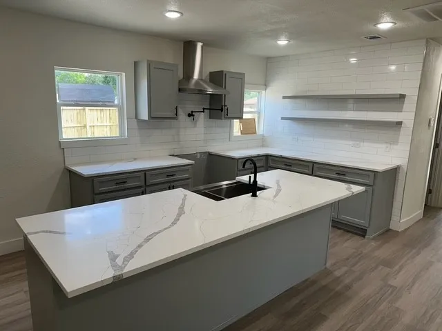 Kitchen featuring gray cabinetry, white countertops with veining, white subway tile backsplash, and stainless steel range hood
