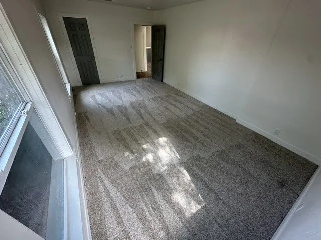 Gray patterned carpet, white walls, and a dark gray door with white trim