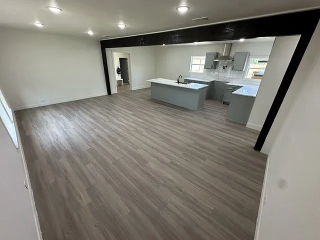 Spacious open-concept layout featuring wood-finish flooring, recessed lighting, a kitchen island with seating, grey cabinetry, and white countertops