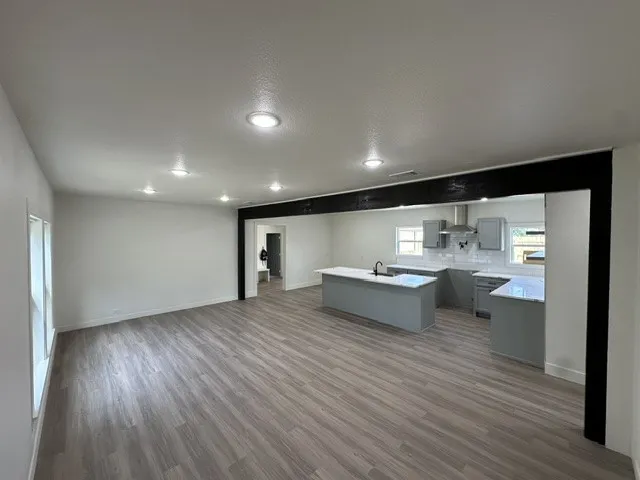 Open-concept living space with wood-finish flooring, recessed lighting, and a kitchen featuring a central island, grey cabinetry, and stainless steel appliances