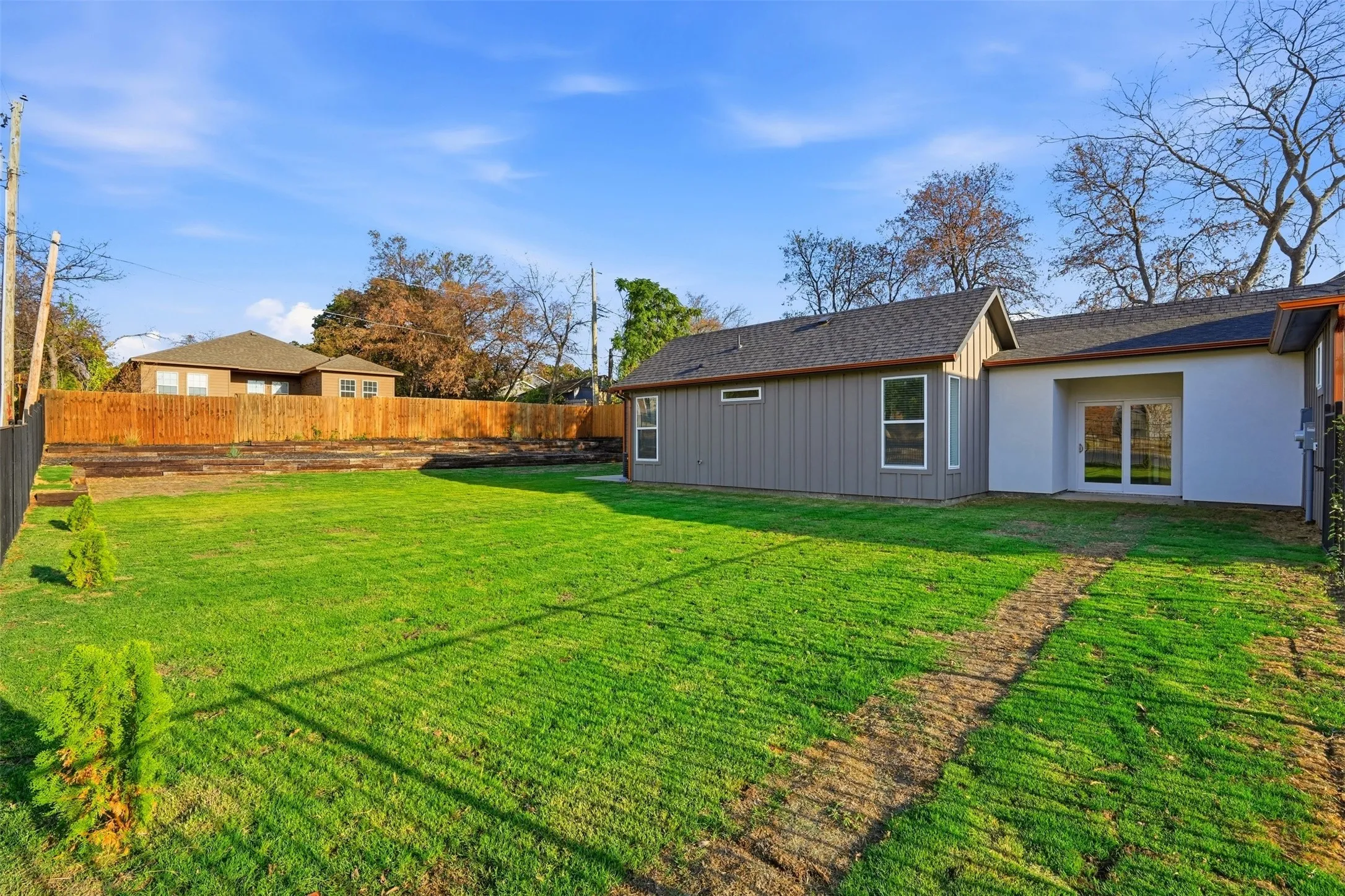 Expansive backyard featuring a manicured lawn, wood fencing, and a contemporary exterior with sliding glass doors