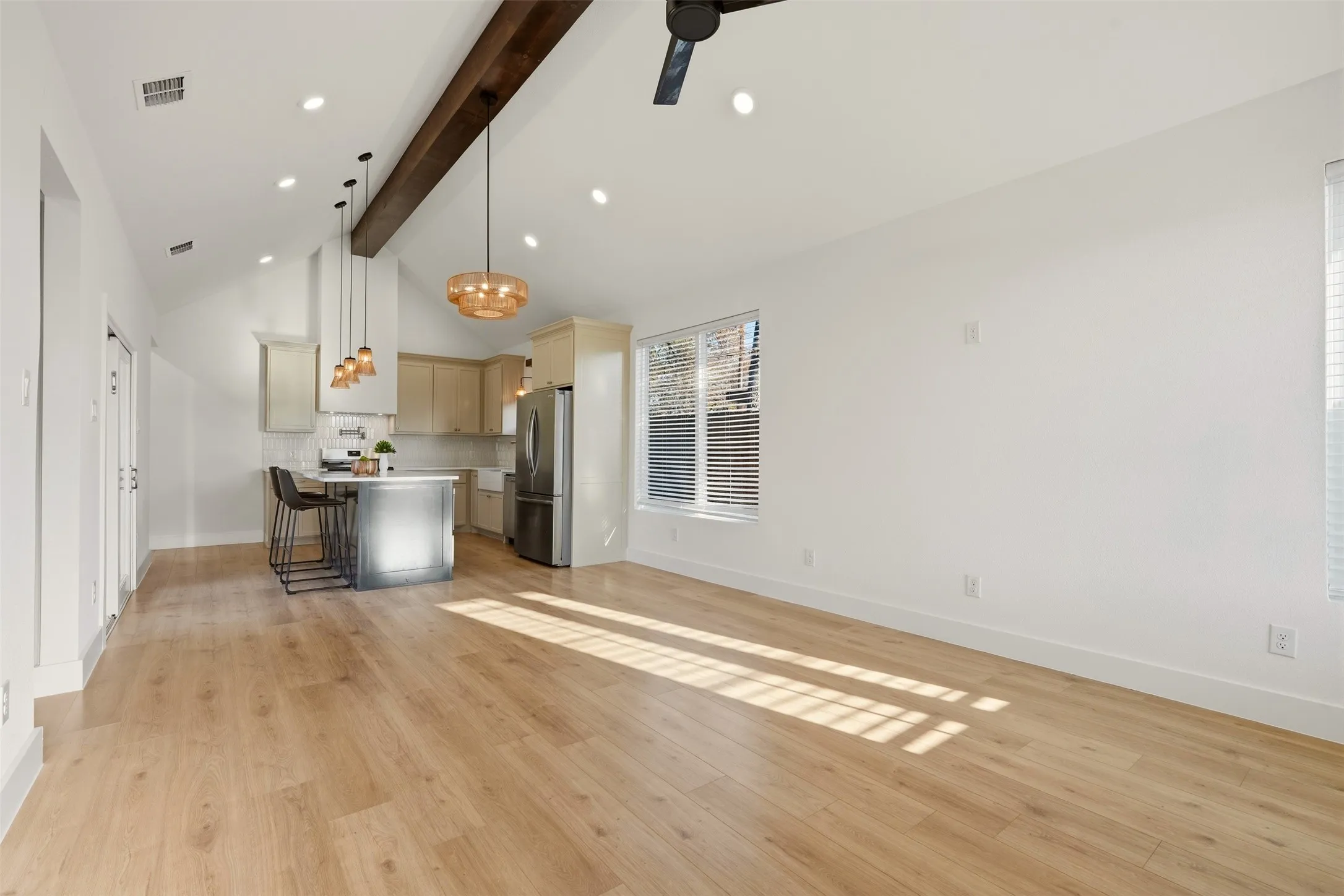 Vaulted ceiling with an exposed wood beam, recessed lighting, wood-finish flooring, and a kitchen island with pendant lighting