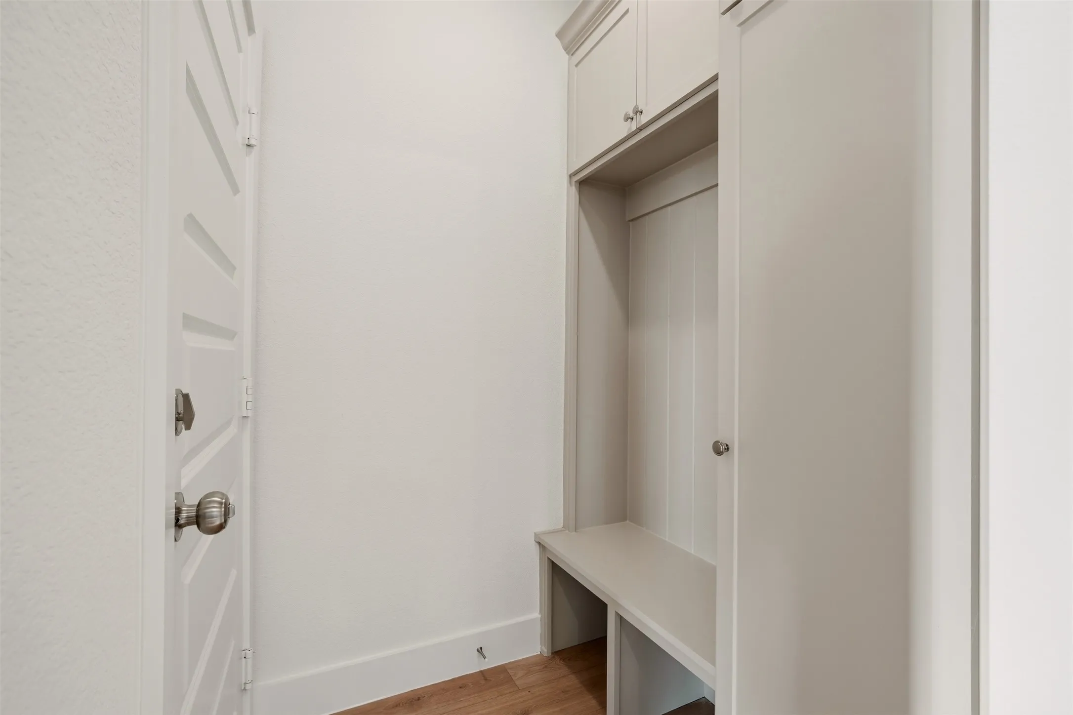 Built-in mudroom bench with upper cabinetry, wood-finish flooring, and a white paneled door