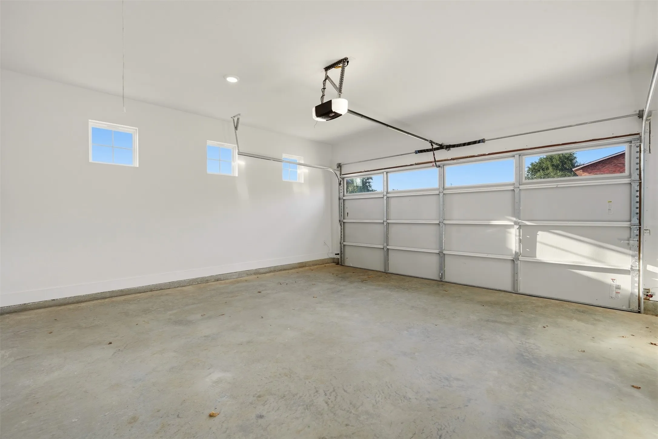 Attached two-car garage with a concrete floor, three high-set rectangular windows, and a segmented garage door with upper window panels