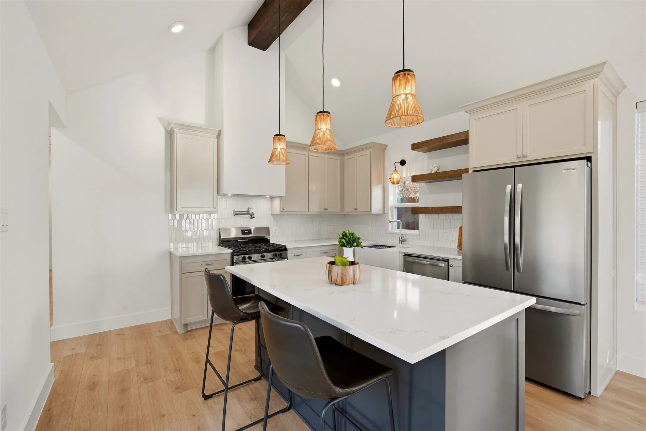 Vaulted ceiling with exposed wood beam, kitchen island with solid surface countertop, wood-finish flooring, stainless steel appliances, and white tile backsplash