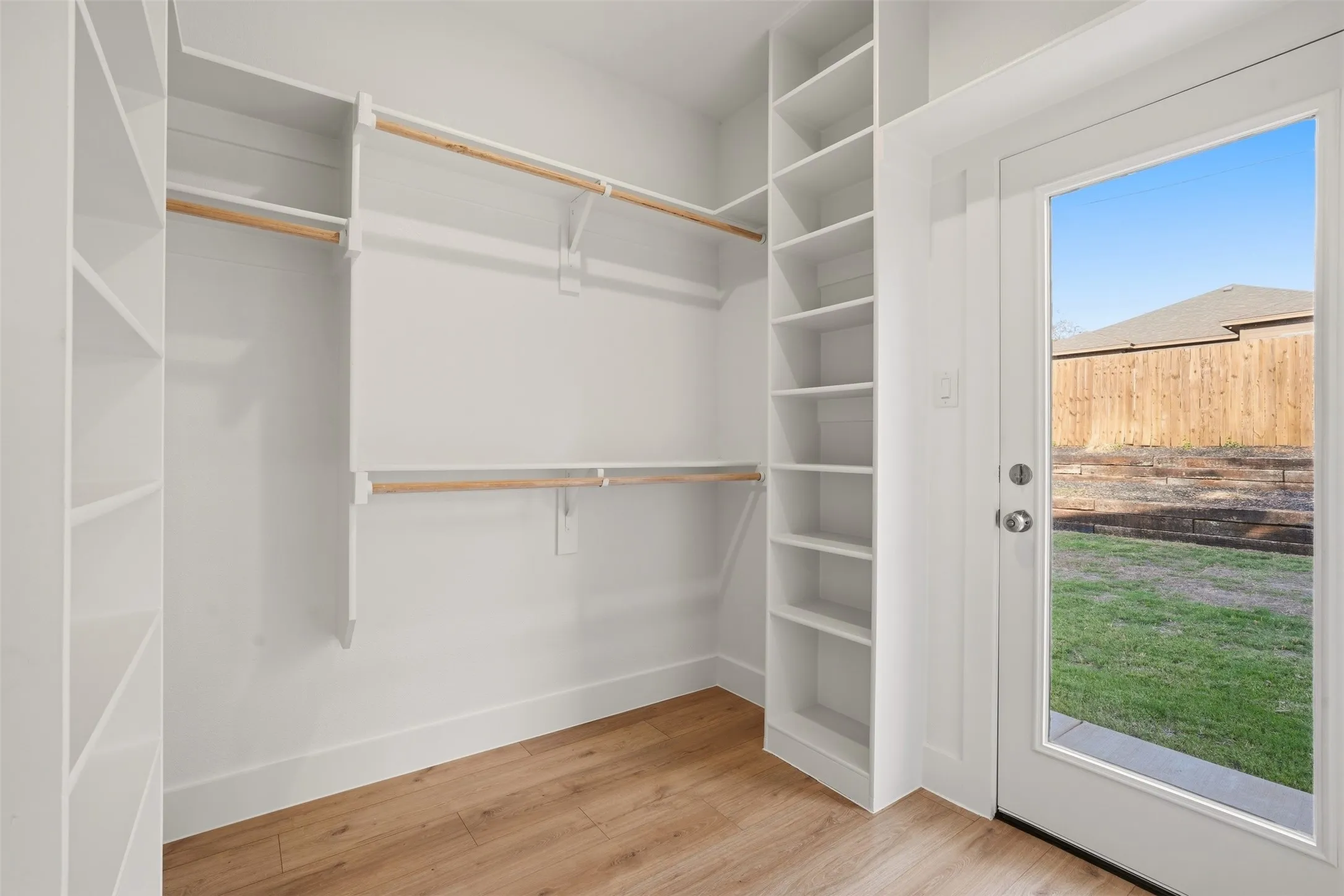 White built-in shelving, natural wood finish hanging rods, wood-finish flooring, and a glass-paneled door