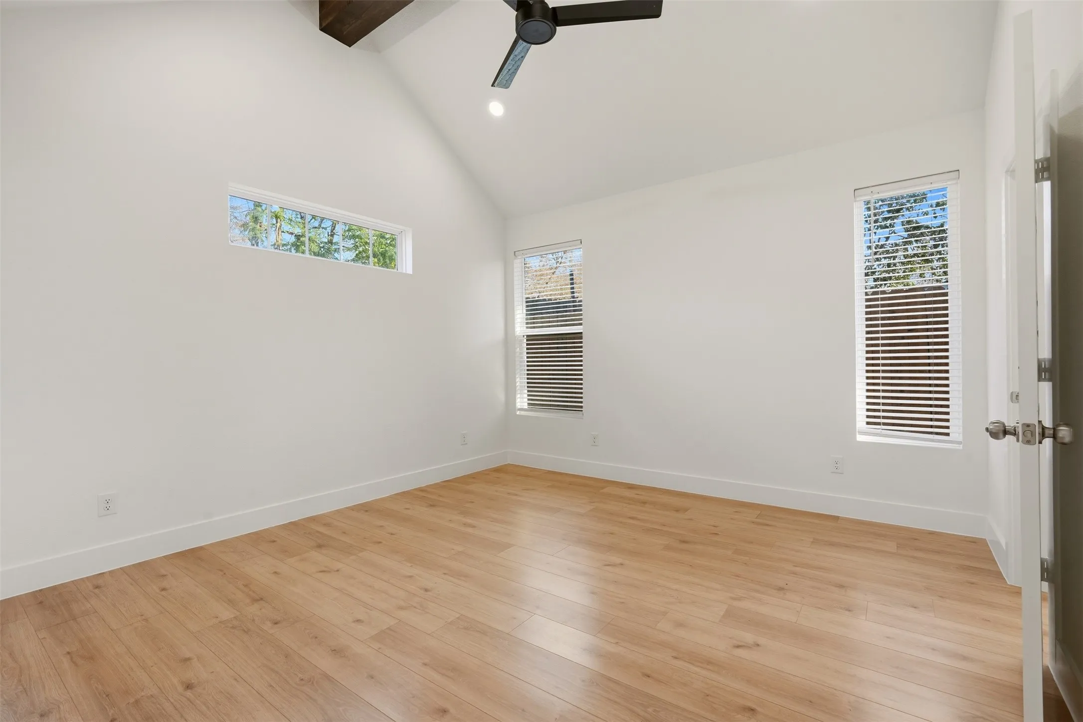 Vaulted ceiling with exposed wood beam, wood-finish flooring, multiple windows, and a ceiling fan