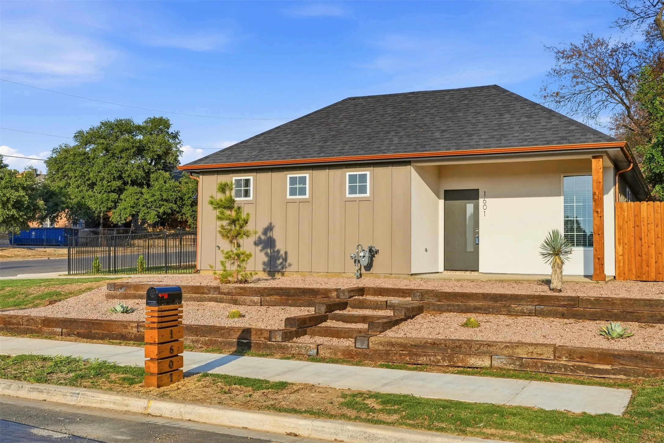 Contemporary exterior with board-and-batten siding and stucco, dark shingle roof, and a wood-slat privacy fence