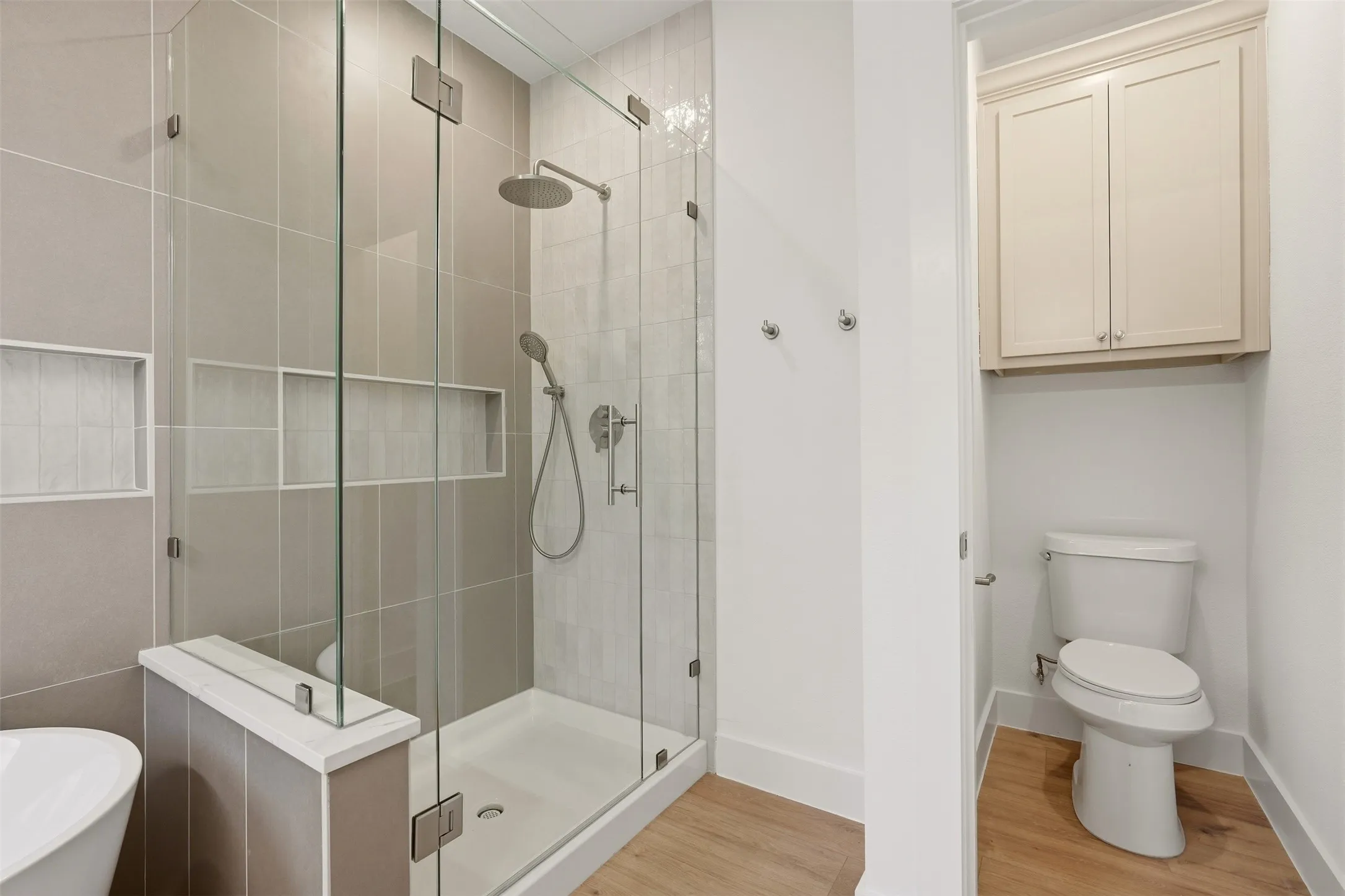Glass-enclosed shower with a rainfall showerhead, handheld sprayer, and integrated wall niches