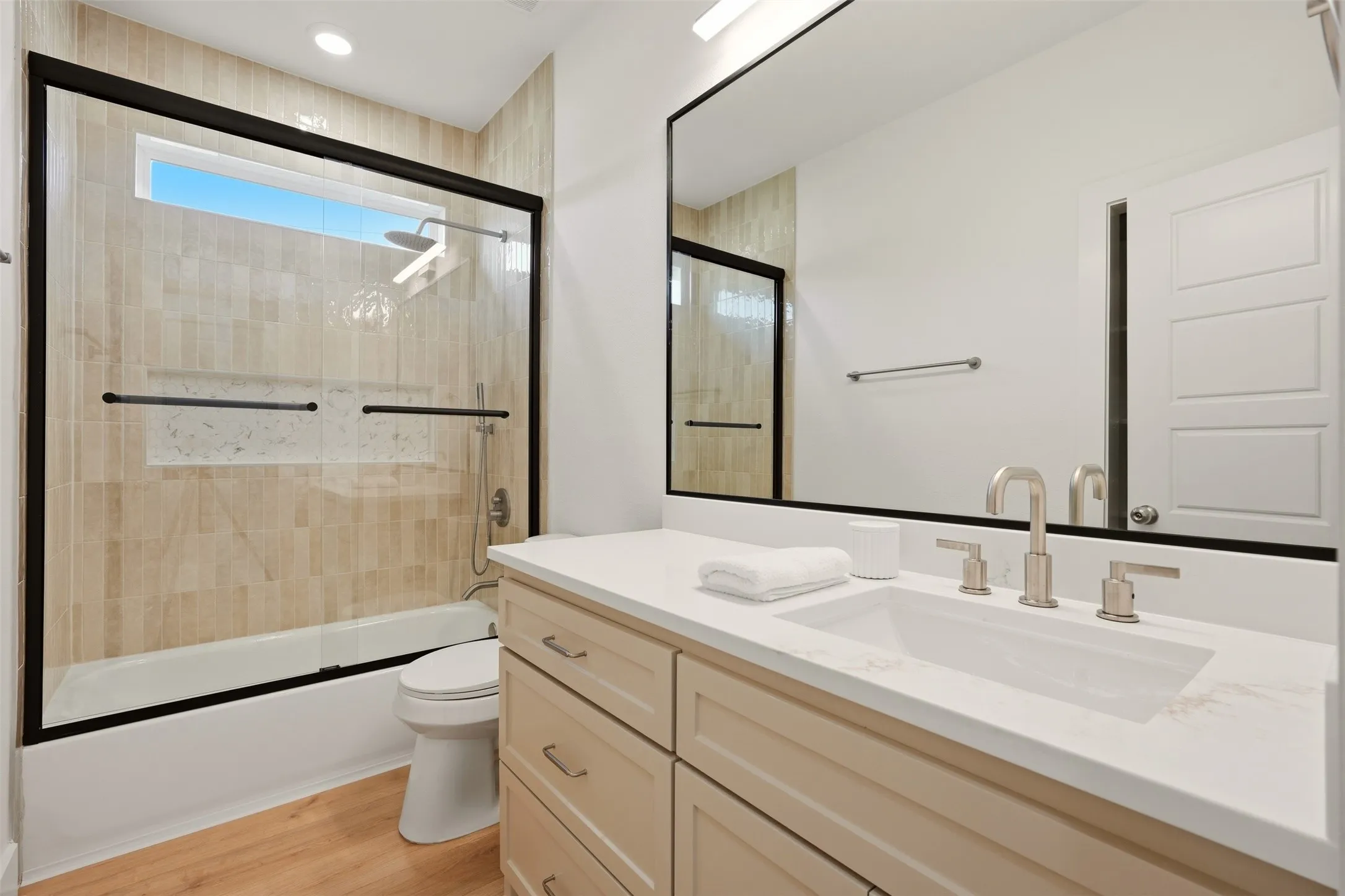 Floating vanity with a rectangular undermount sink, brushed nickel faucet, large frameless mirror, and a shower-tub combination with tile surround