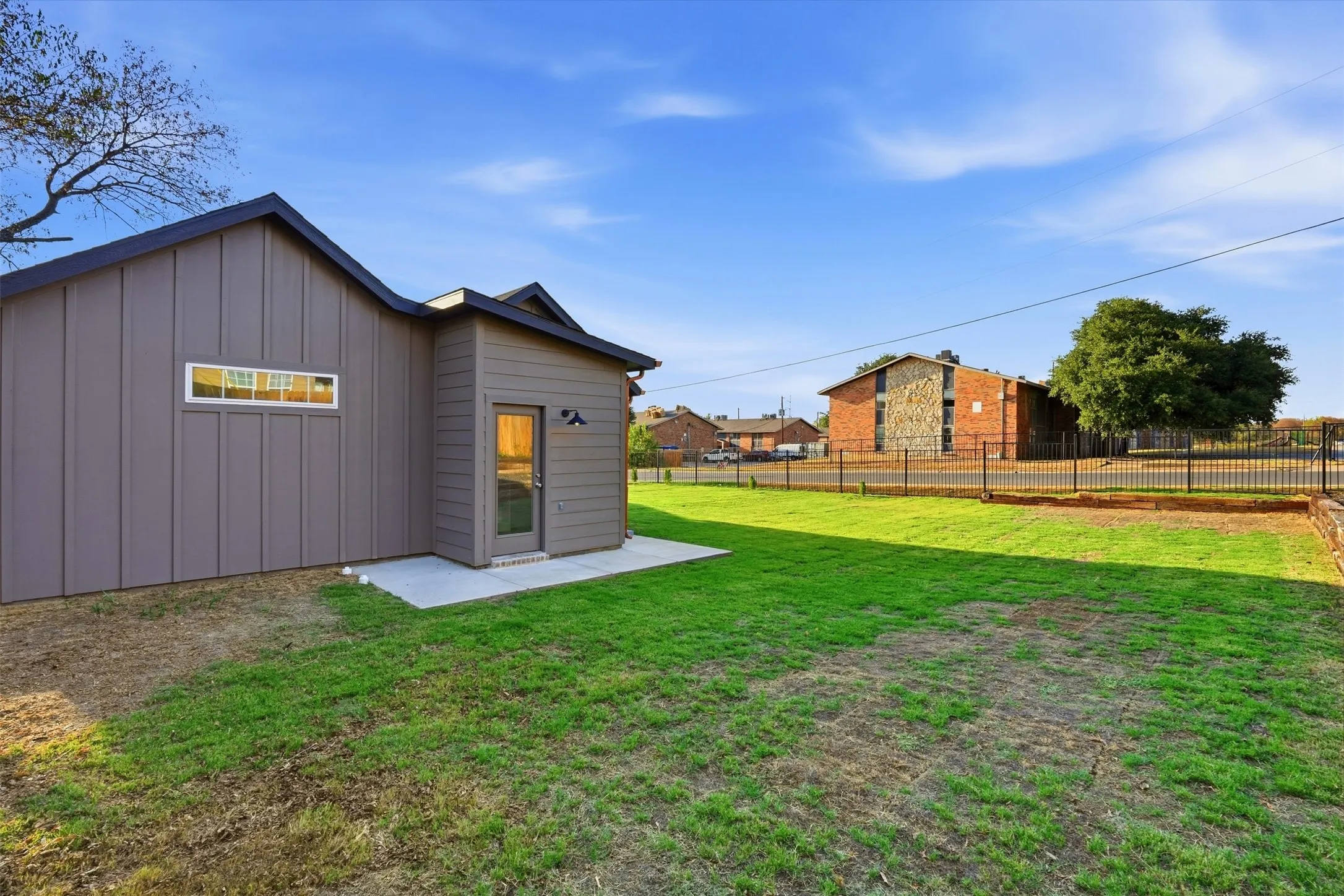 Manicured lawn with a concrete patio and direct access door, featuring board and batten siding and a horizontal window
