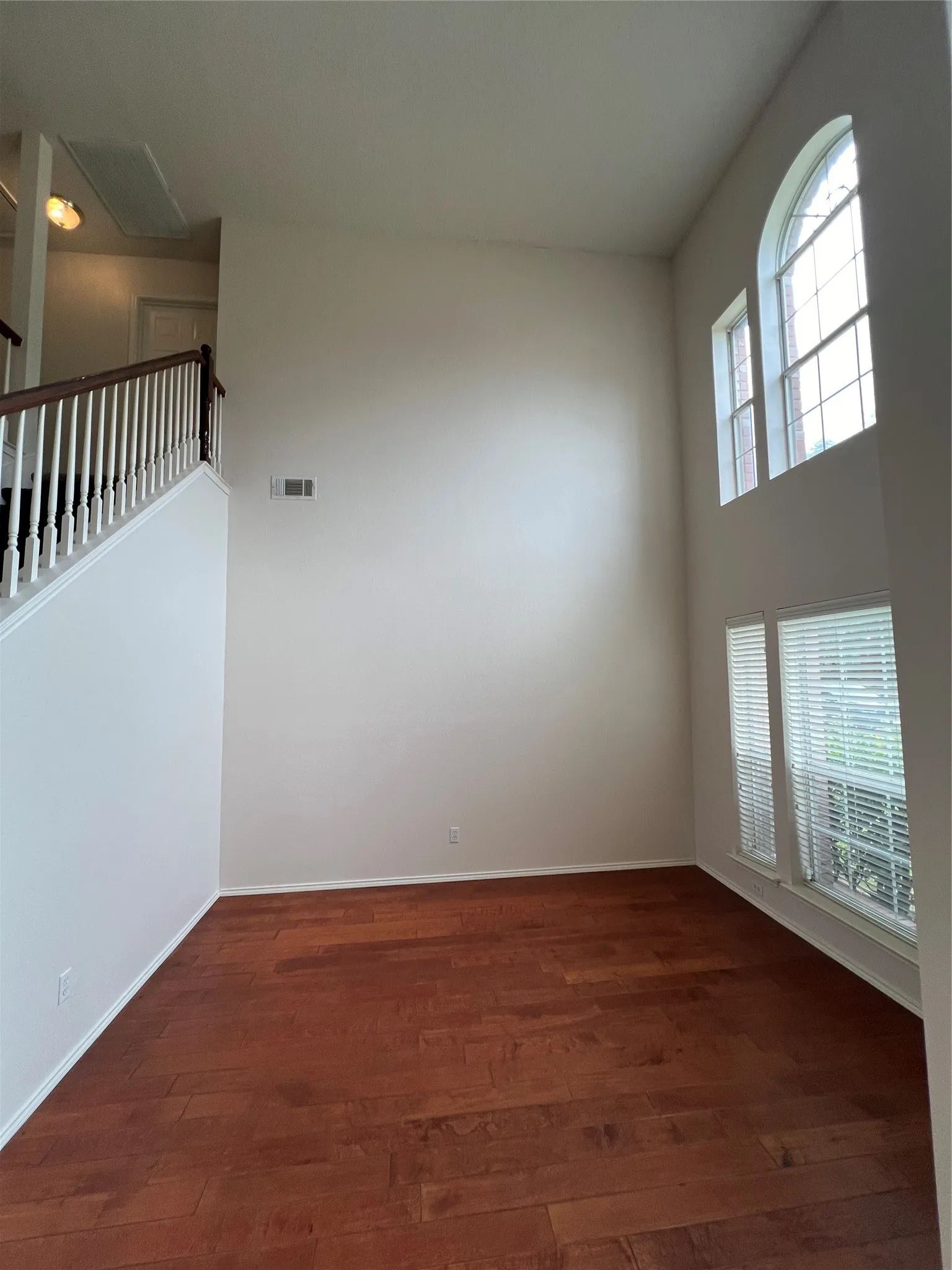 High ceilings with an arched window and additional windows, wood-finish flooring, and a staircase with white spindles and a wood handrail