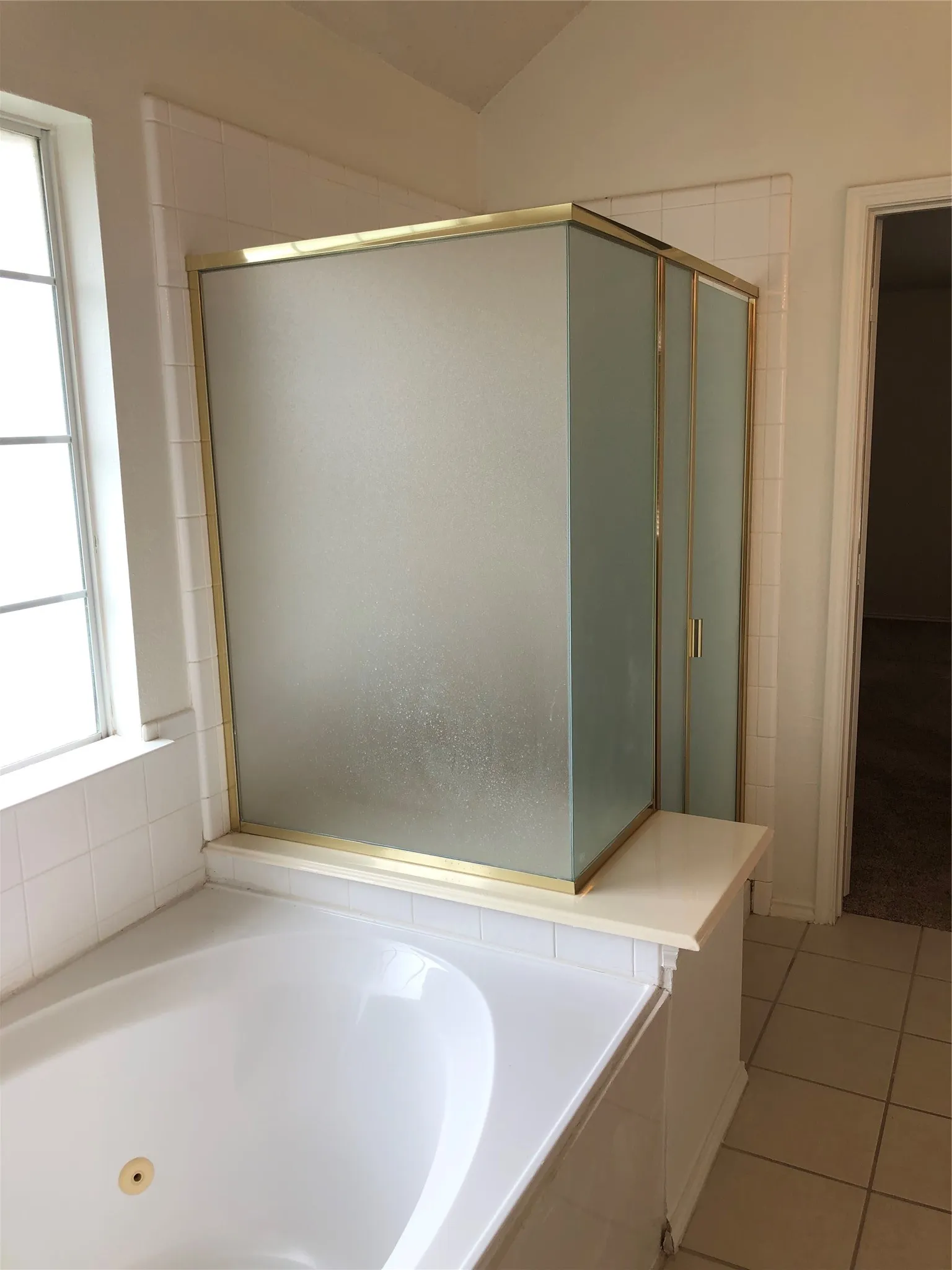 Built-in soaking tub, shower enclosure with frosted glass panels, brass-finish shower frame, ceramic tile flooring, and vaulted ceiling