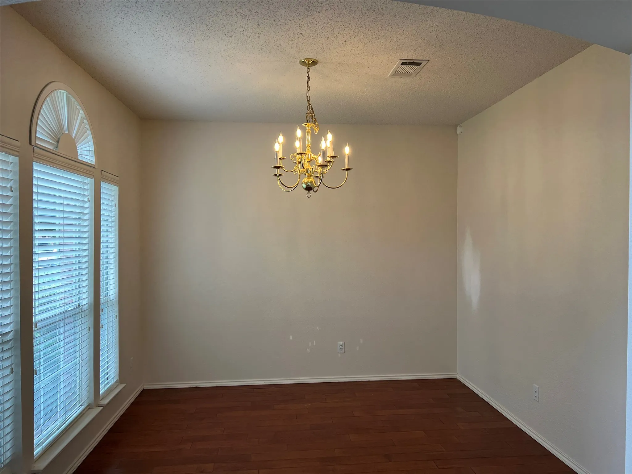 Arch-top window with blinds, wood-finish flooring, and a chandelier