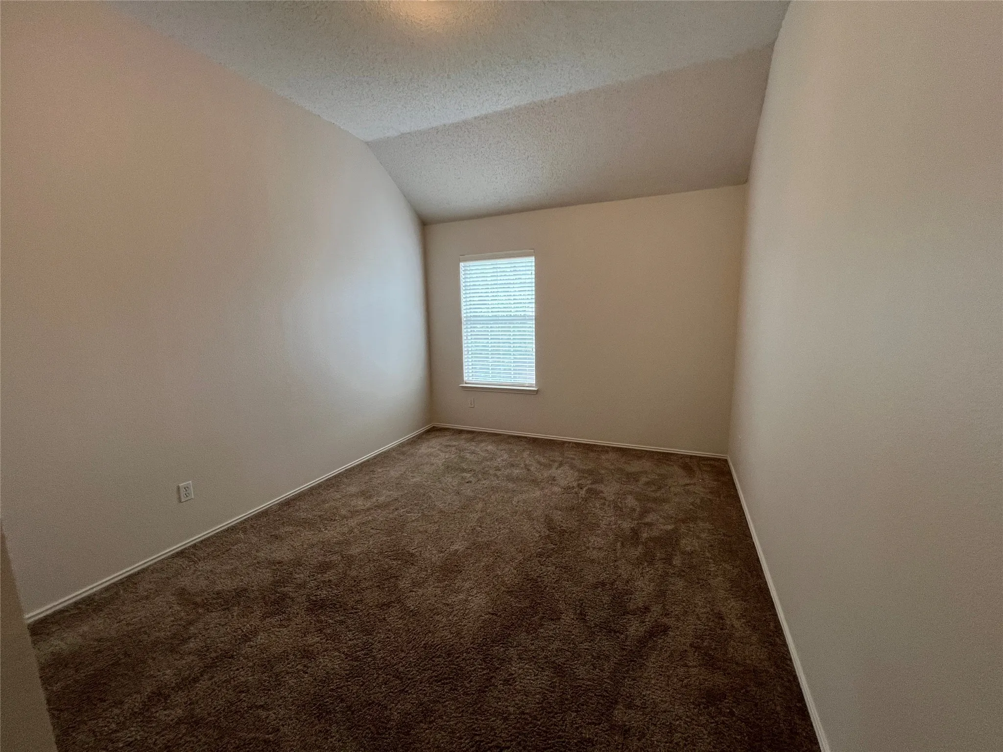 Neutral paint walls with textured finish, sloped ceiling, window with blinds, and brown carpet flooring