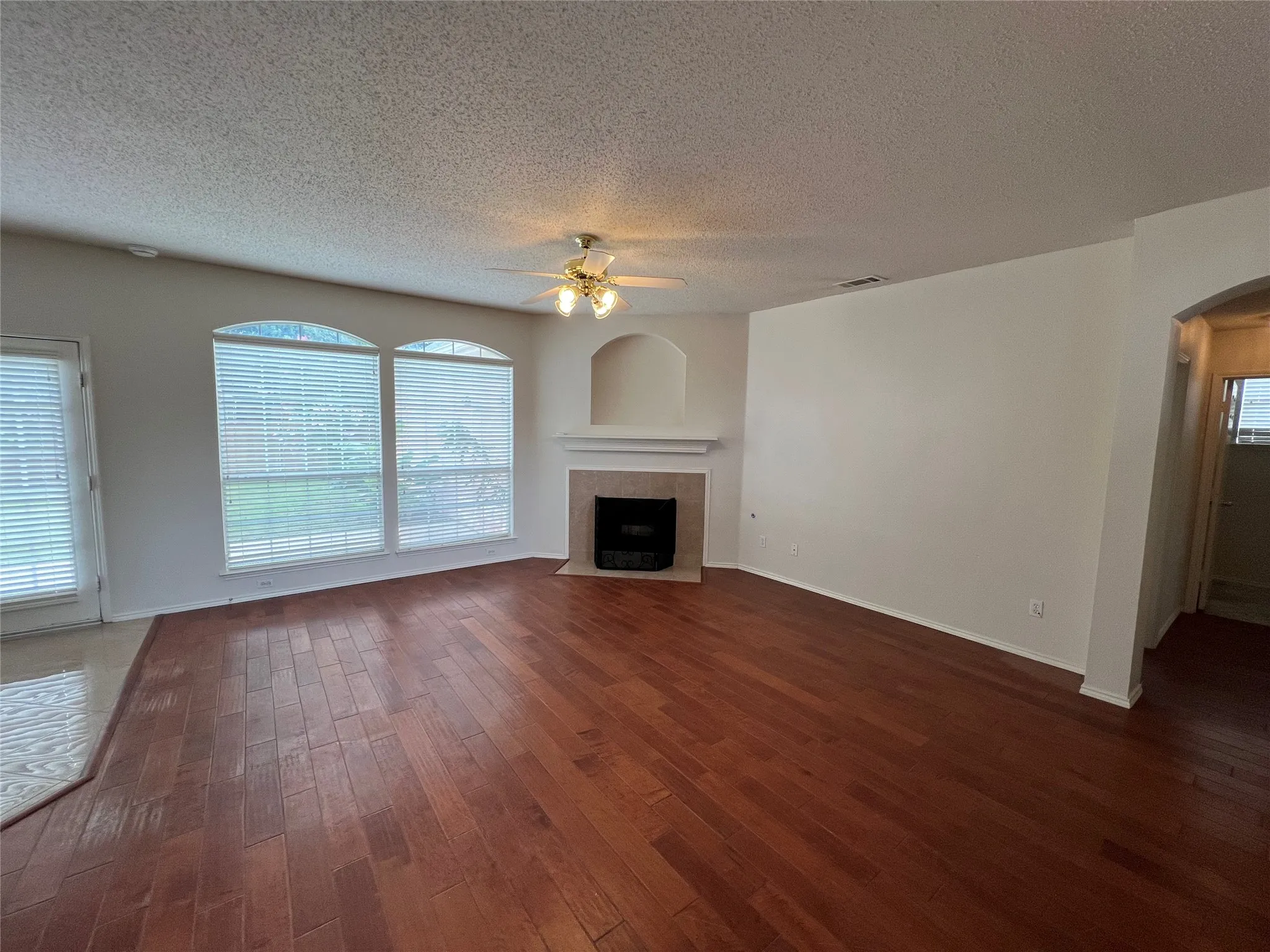Expansive room featuring wood-finish flooring, a ceiling fan, and a fireplace with a mantel