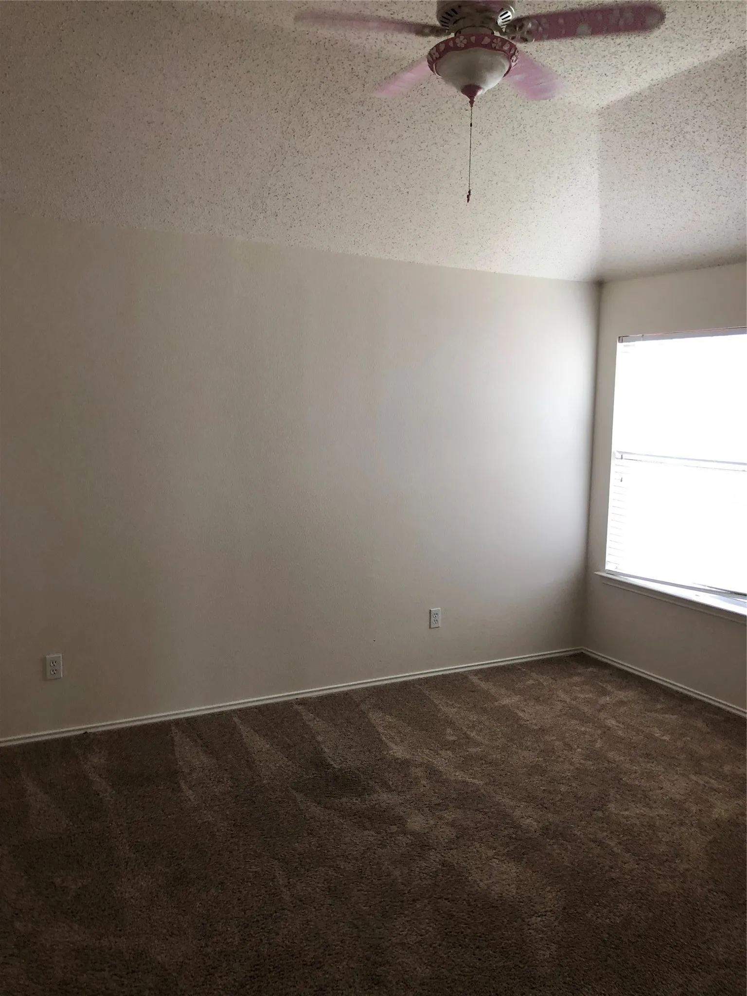 Wall-to-wall carpeting with light-toned walls, featuring a window with blinds and a ceiling fan