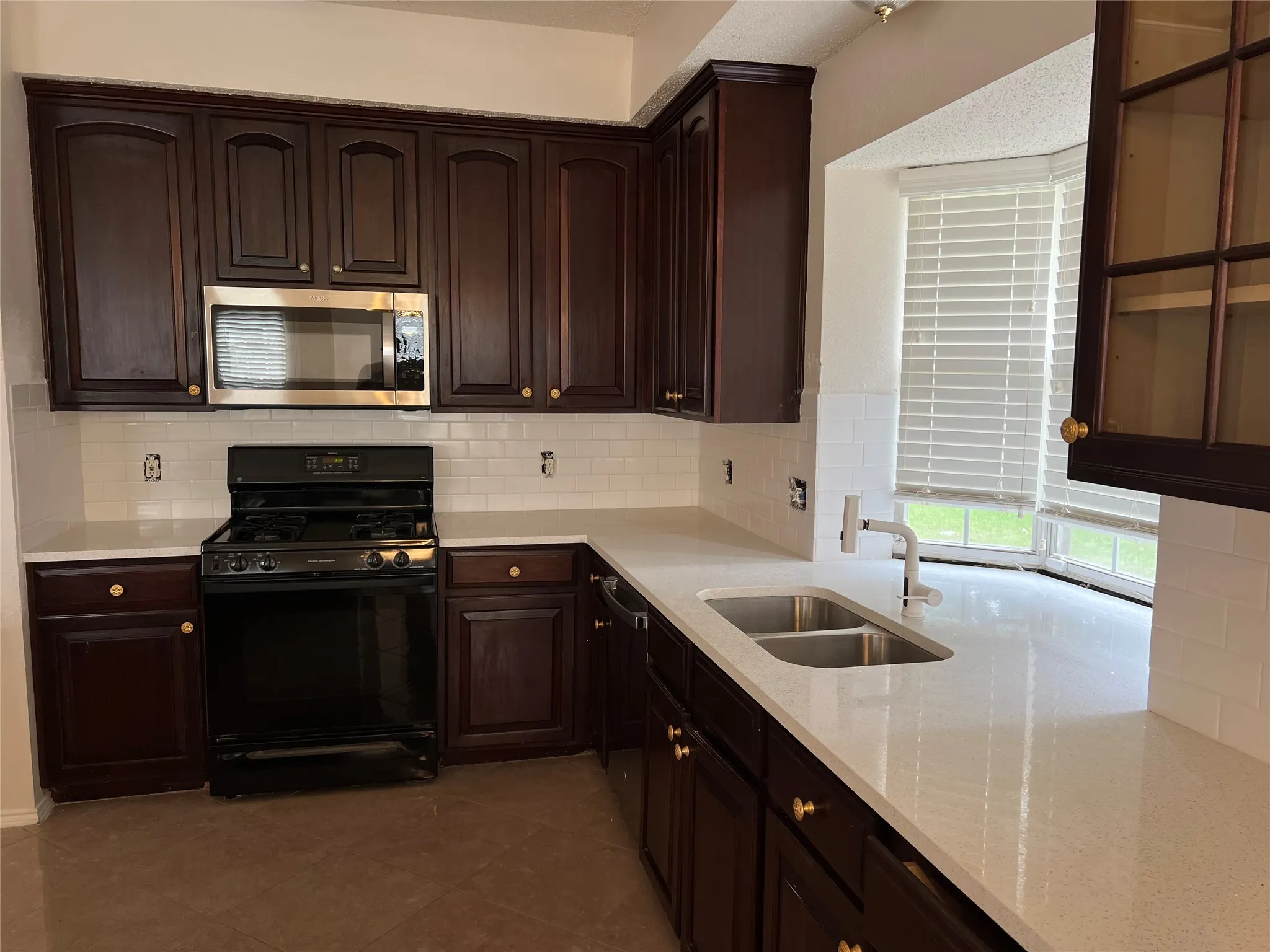 Kitchen featuring dark wood cabinetry, white countertops, white subway tile backsplash, a stainless steel microwave, and a double basin sink with a gooseneck faucet