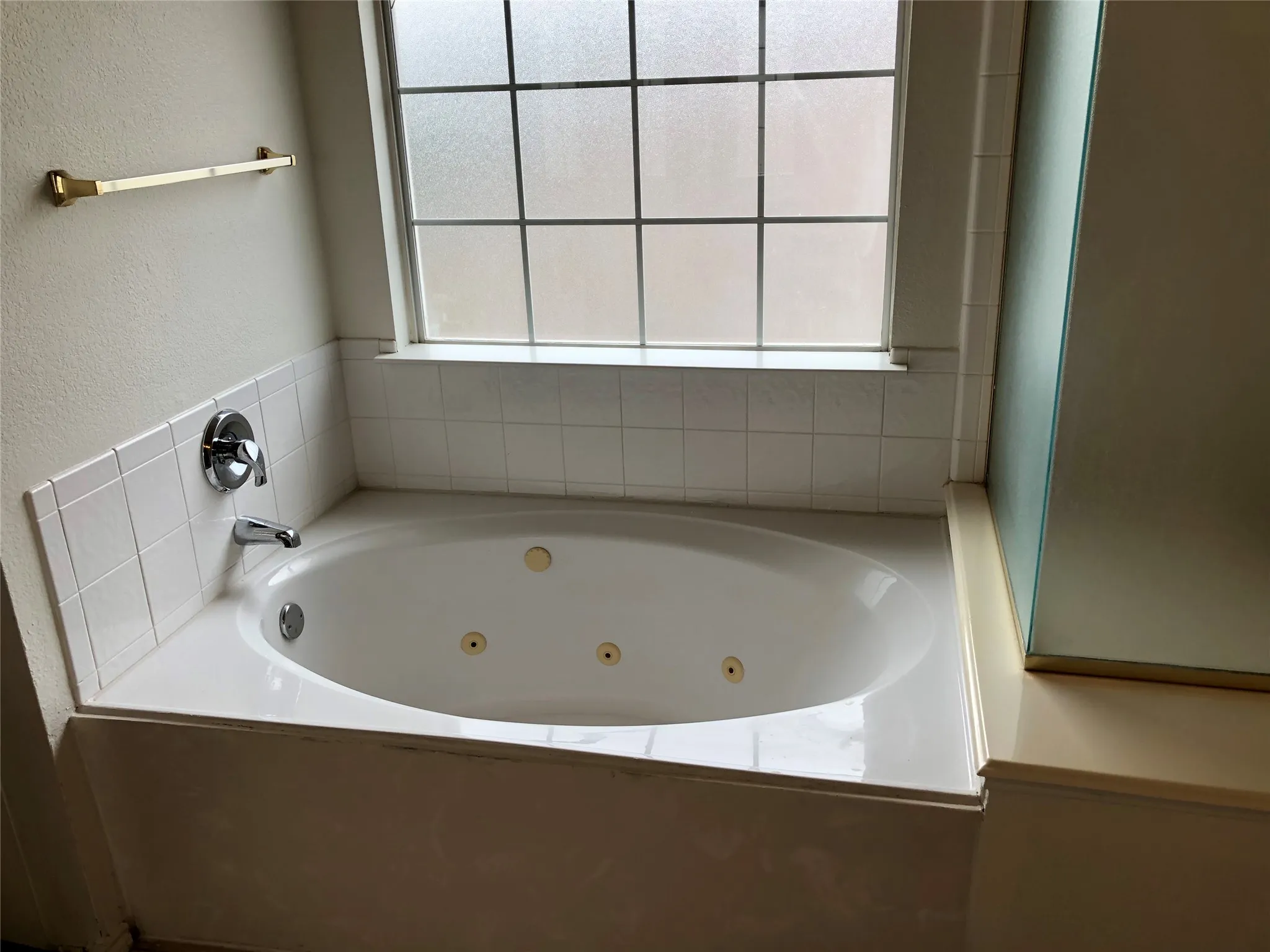 Built-in jetted tub with polished chrome fixtures, white tile surround, and privacy window