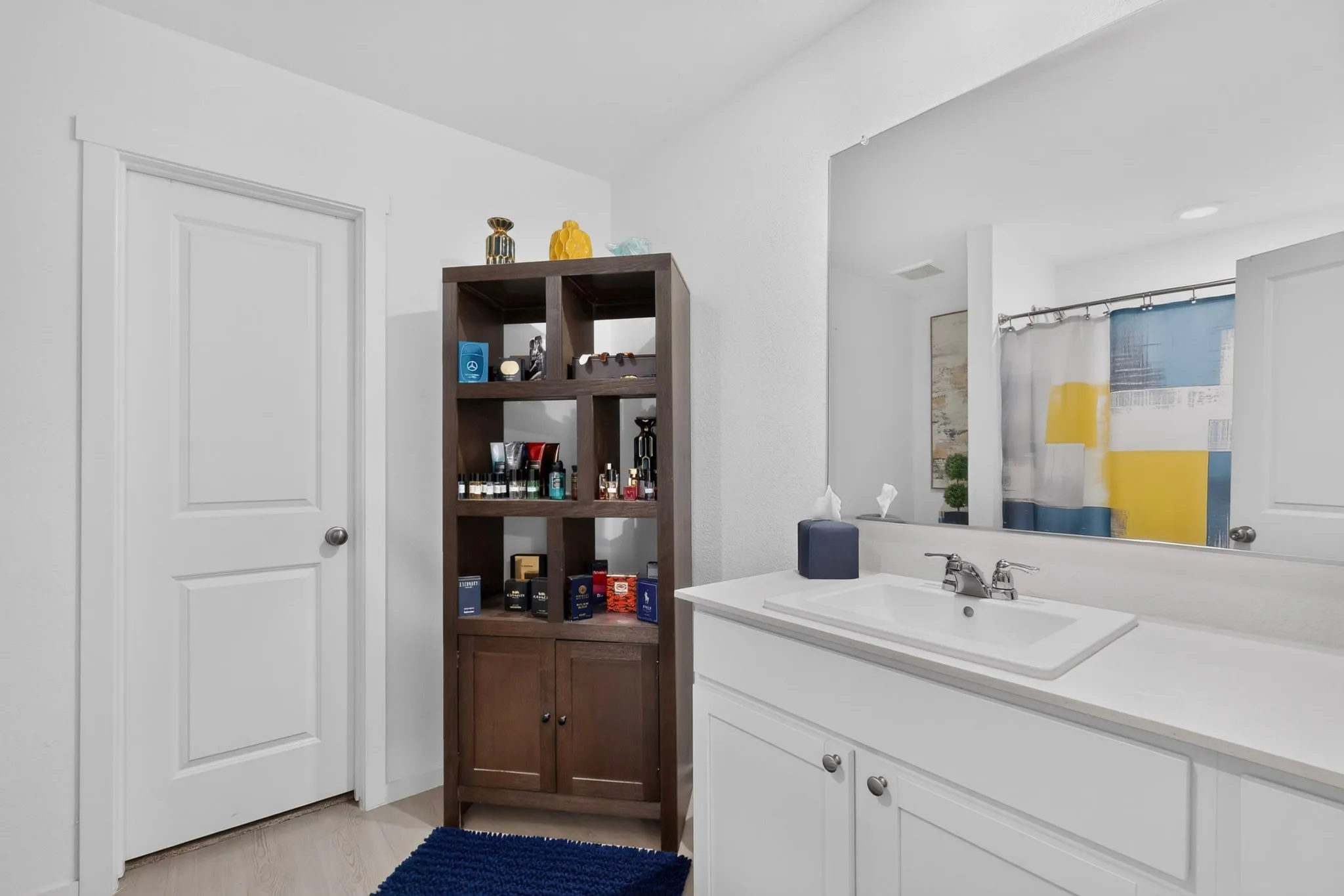 White paneled door, wood-finish shelving unit, white vanity with integrated sink, chrome faucet, and expansive wall mirror