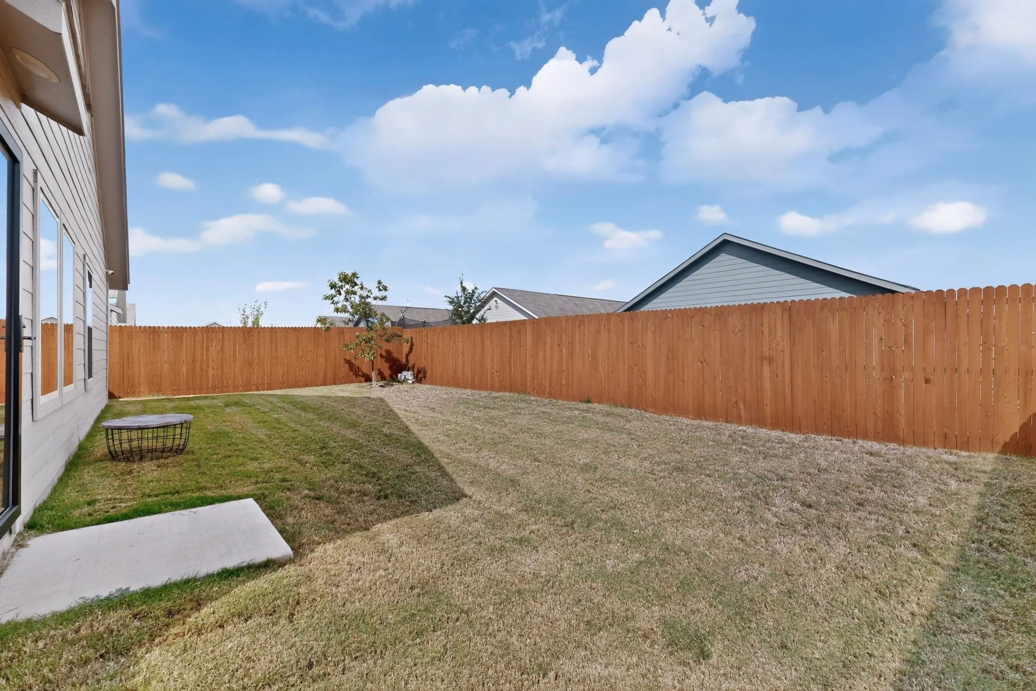 Expansive backyard featuring a new wood privacy fence, concrete patio, and a light-colored exterior wall with multiple windows